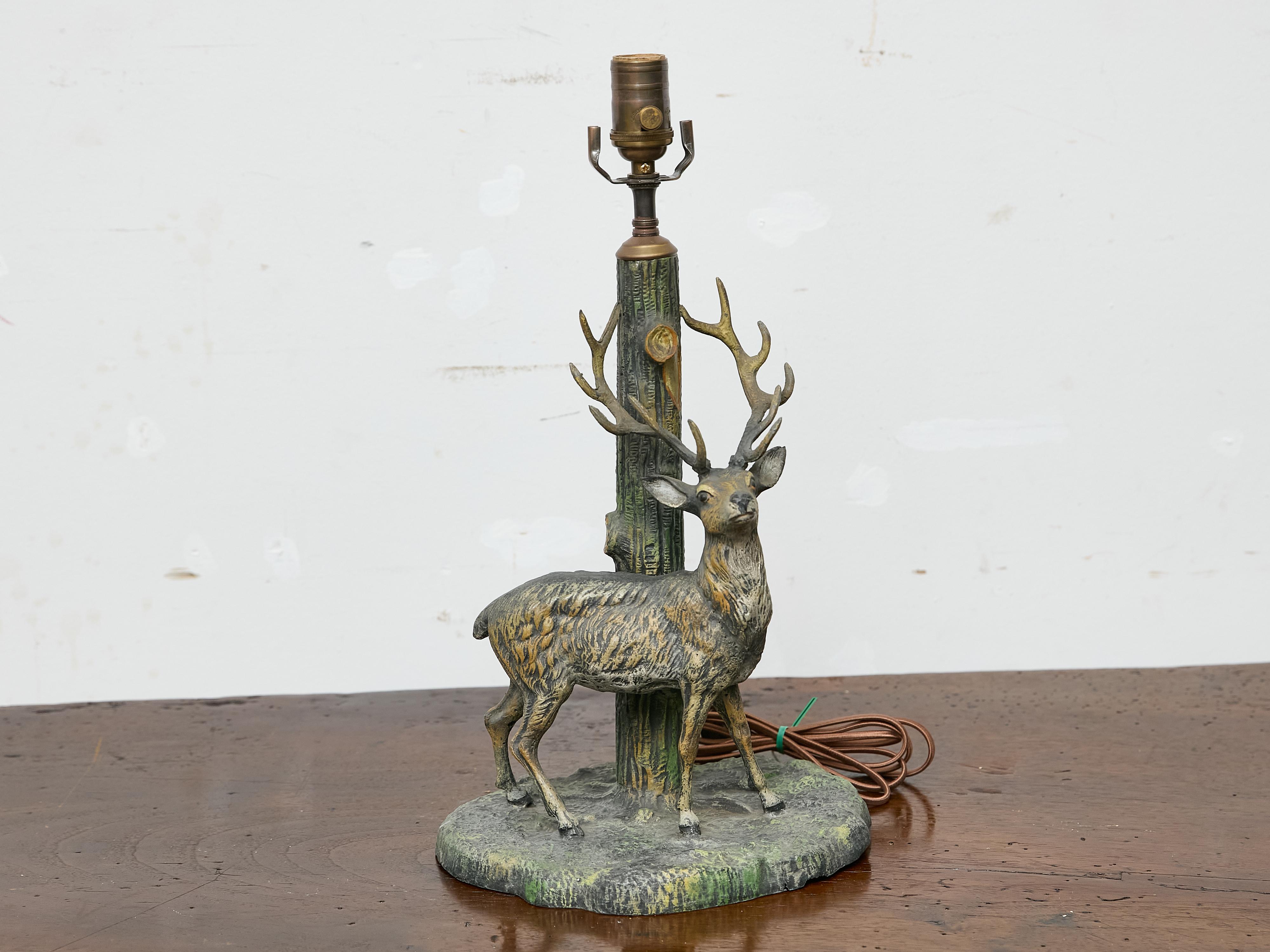 This table lamp features a 19th-century American cast metal sculpture of a stag that has been thoughtfully repurposed as a lighting piece. The proud stag is depicted standing alert at the base of a textured tree trunk, which now supports the lamp’s