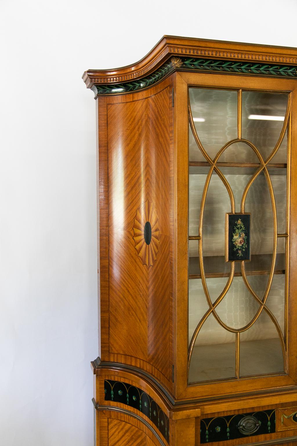 American Adam style satinwood cabinet, has curved window muntins with floral painted center panels. The lower portion has bookmatched satinwood veneer and interior pull our shelves, the entirety painted in the style of Robert Adam.
   