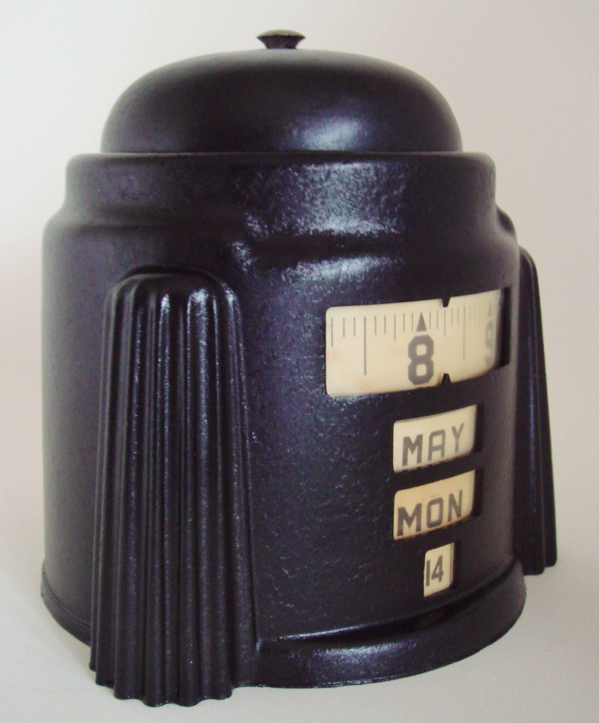 This American Art Deco Kal-Klock black wrinkle painted mechanical alarm clock with integral manual tape-measure type perpetual calendar was designed and patented (Des 110,489 please see below) by Herbert W. Lamport in 1938. It would seem that he