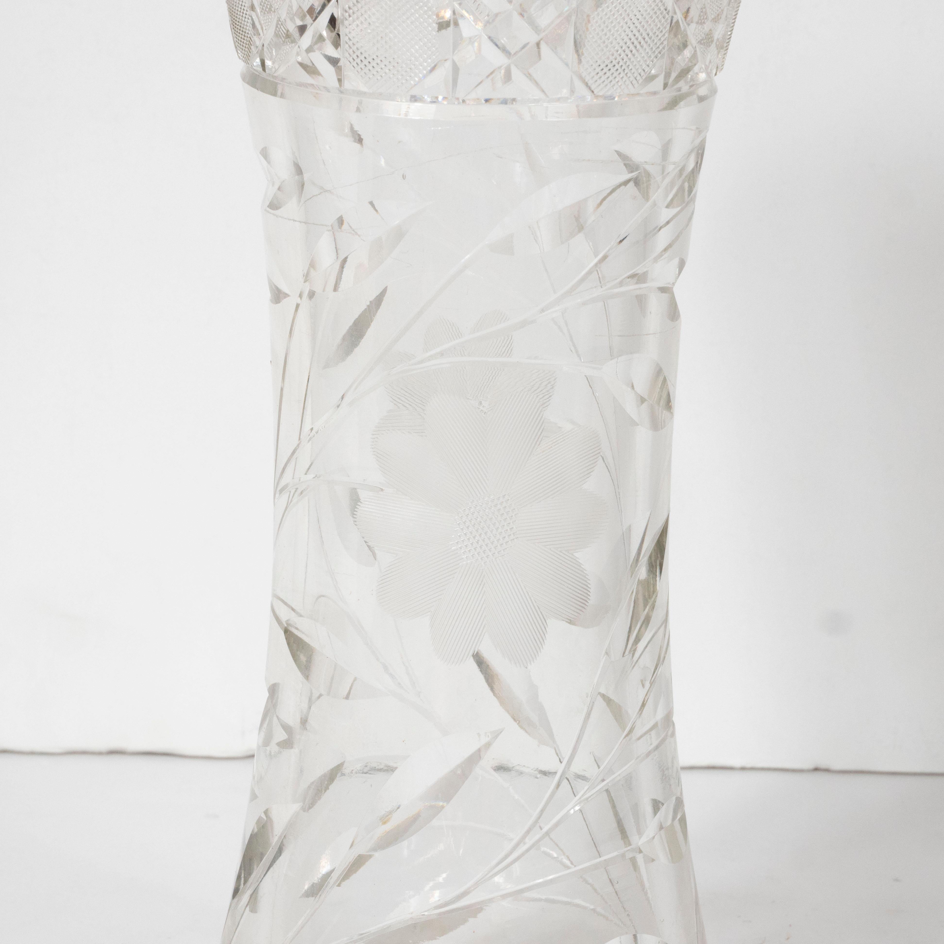 This beautiful brilliant cut glass vase was realized in the United States, circa 1920. It offers an austere hourglass form; an intricately cut neck with an abundance of geometric patternation; as well as floral designs etched into the translucent