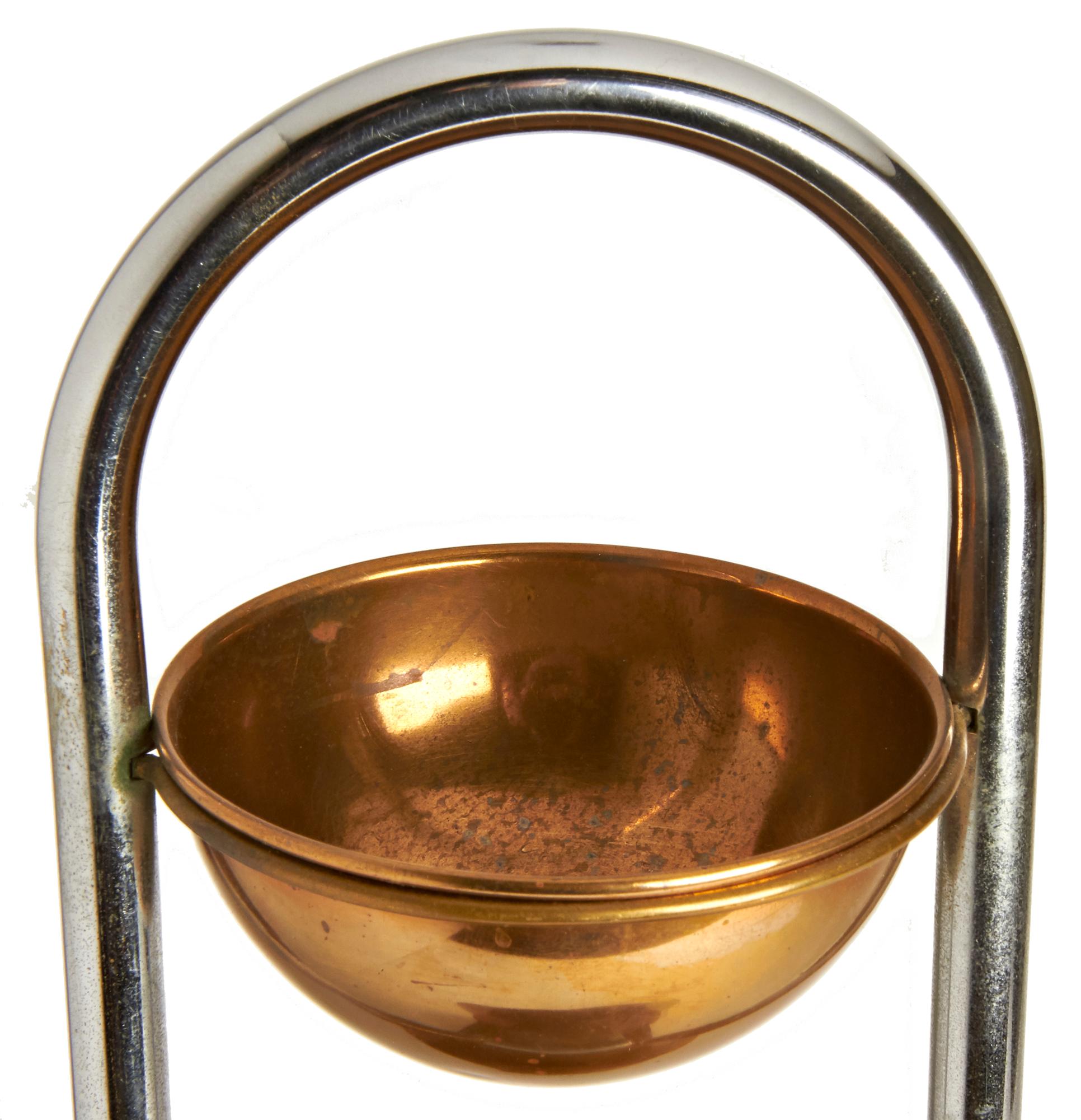 This iconic American Art Deco chrome, copper and lacquered wood combination ashtray and magazine stand was designed by William Archibald Welden for Revere. A tubular chrome arch shaped handle rises from a black lacquered wood base with a chamfered