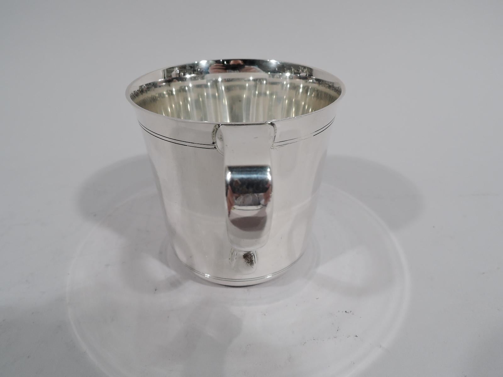 Art Deco sterling silver baby cup. Made by Tiffany & Co. in New York, ca 1941. Straight sides with flared rim and scroll bracket handle. Engraved double line borders at top and bottom leave plenty of room for a big-hearted presentation. Fully marked