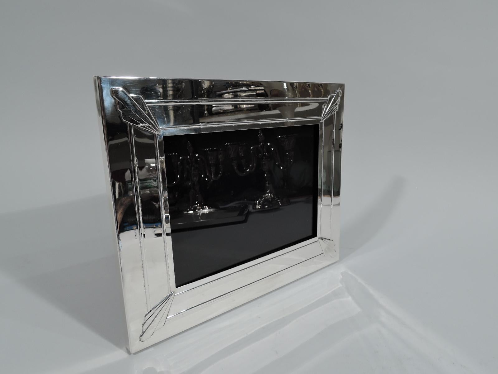 Sharp and Modern sterling silver picture frame. Made by Lunt in Greenfield, Mass, circa 1940. Rectangular window and wide surround with two raised wraparound bands and skyscraper arrows applied at corners. With glass, black lining, and black velvet