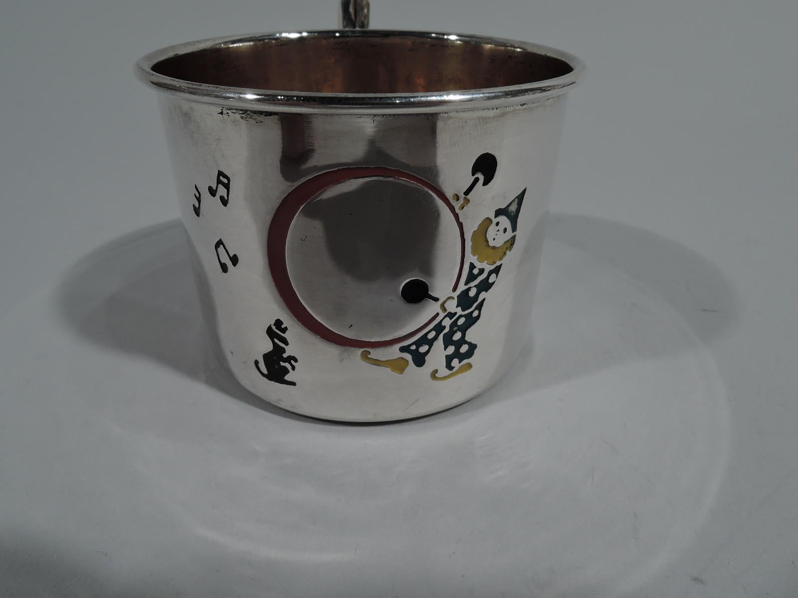 Novelty sterling silver baby cup. Made by Webster in North Attleboro, Mass, circa 1920. Straight sides and high-looping scroll handle. Enameled decoration: A clown pounds away with drumsticks, musical notes emanating to the tune of a very special