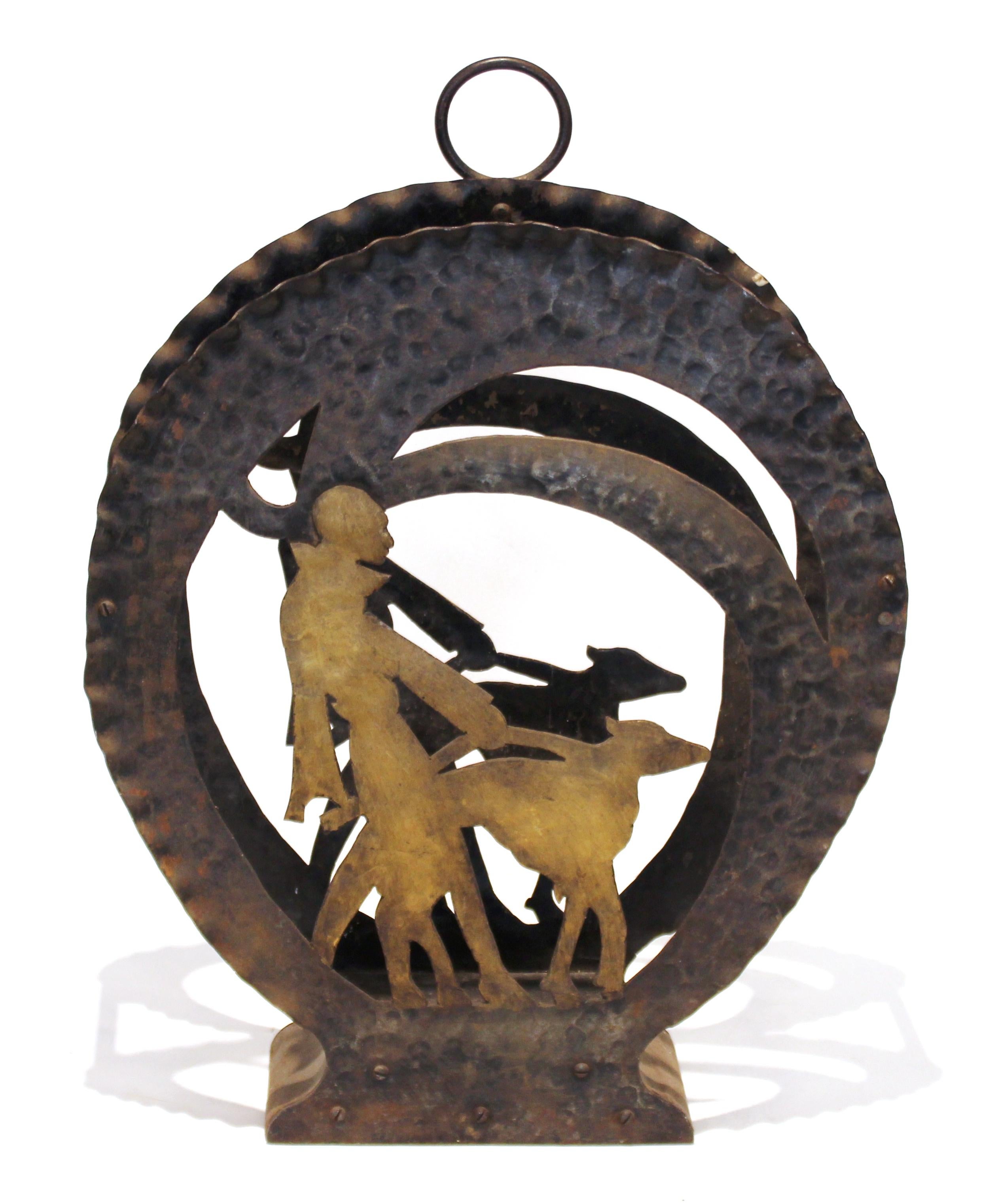 American Art Deco magazine rack made of wrought iron and cutout iron. The central vignette features a silhouette of a lady walking a dog and has a bronze patina. Can stand on floor or be hung on wall. 
In great vintage condition with