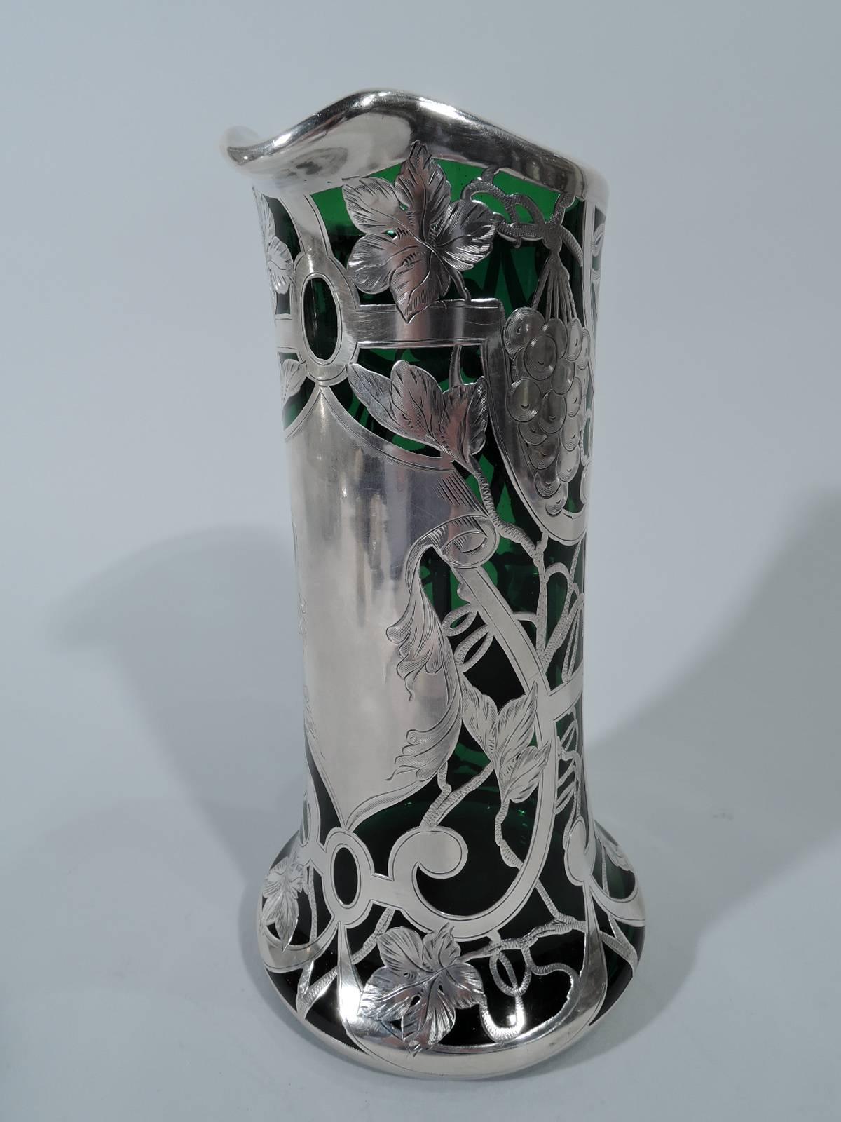 American Art Nouveau emerald glass claret jug with silver overlay. Cylindrical with lip spout, C-scroll handle, and spread base. Strapwork cartouche (vacant) and curvilinear frame entwined with fruiting grapevine. Worn mark.