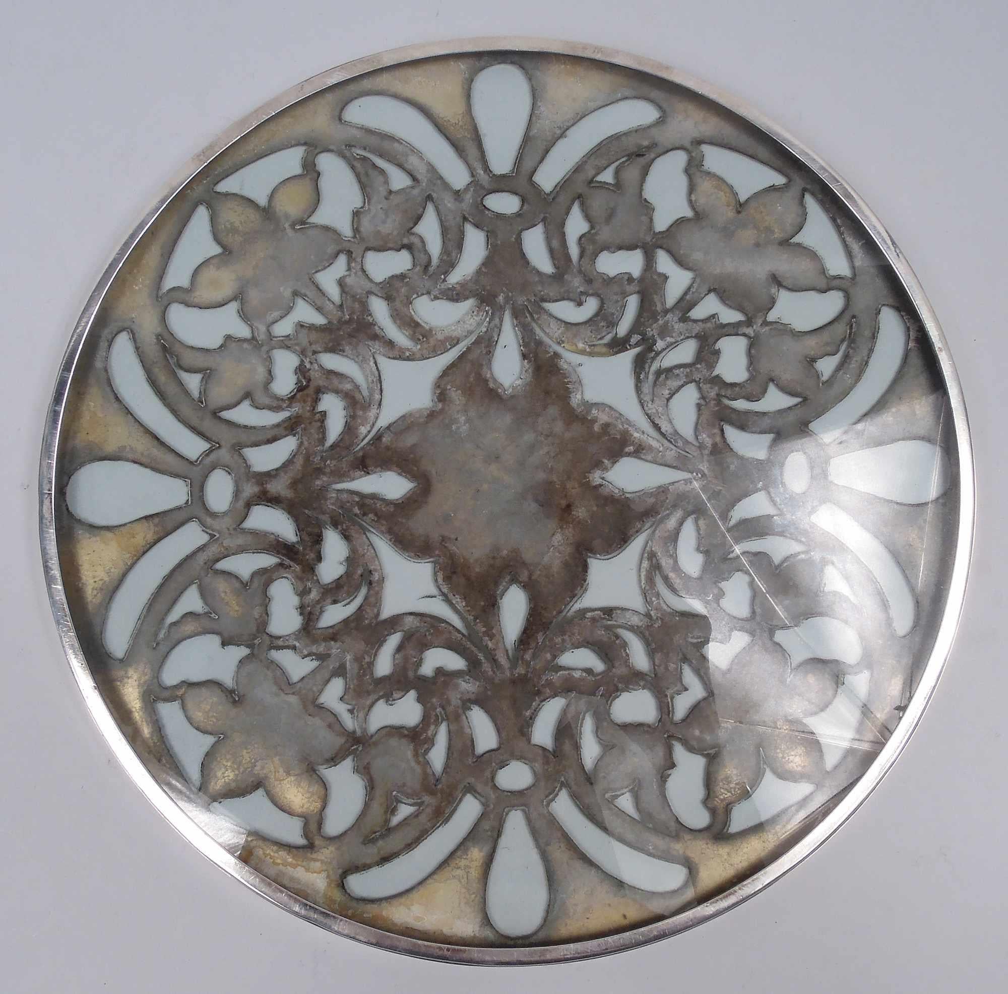 American Art Nouveau glass trivet with engraved silver overlay, ca 1900. Round with straight sides. Overlay in scroll and flower pattern with alternating flowers in round tendril-entwined frames and fleurs de lys. Sold center engraved with