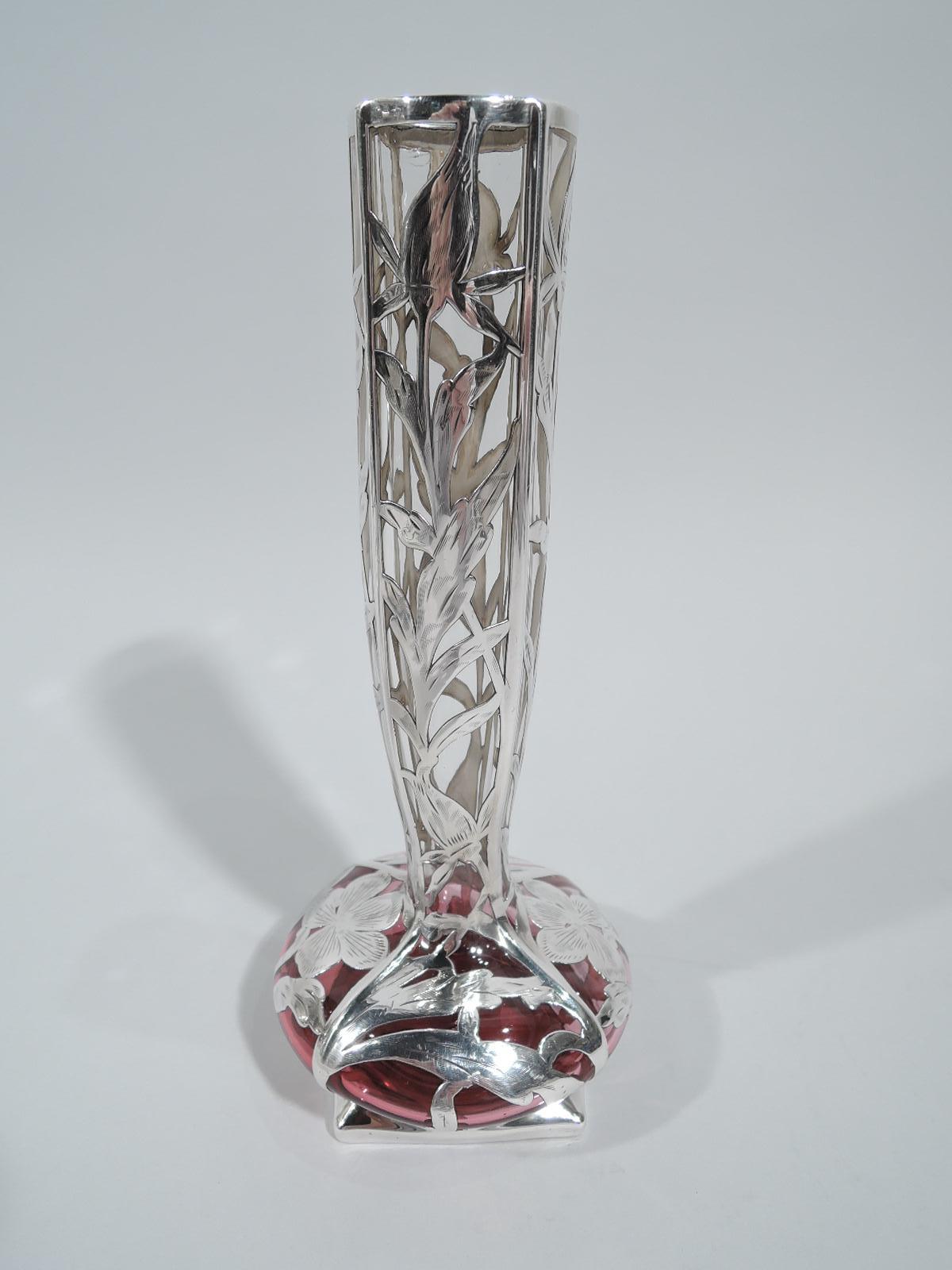 Turn-of-the-century American Art Nouveau vase with engraved silver overlay. Tall and tapering neck with four curved sides, bellied bowl, and square and gently curved base. Floral overlay in ribbed frames. Glass clear shading to cranberry red. Marked.