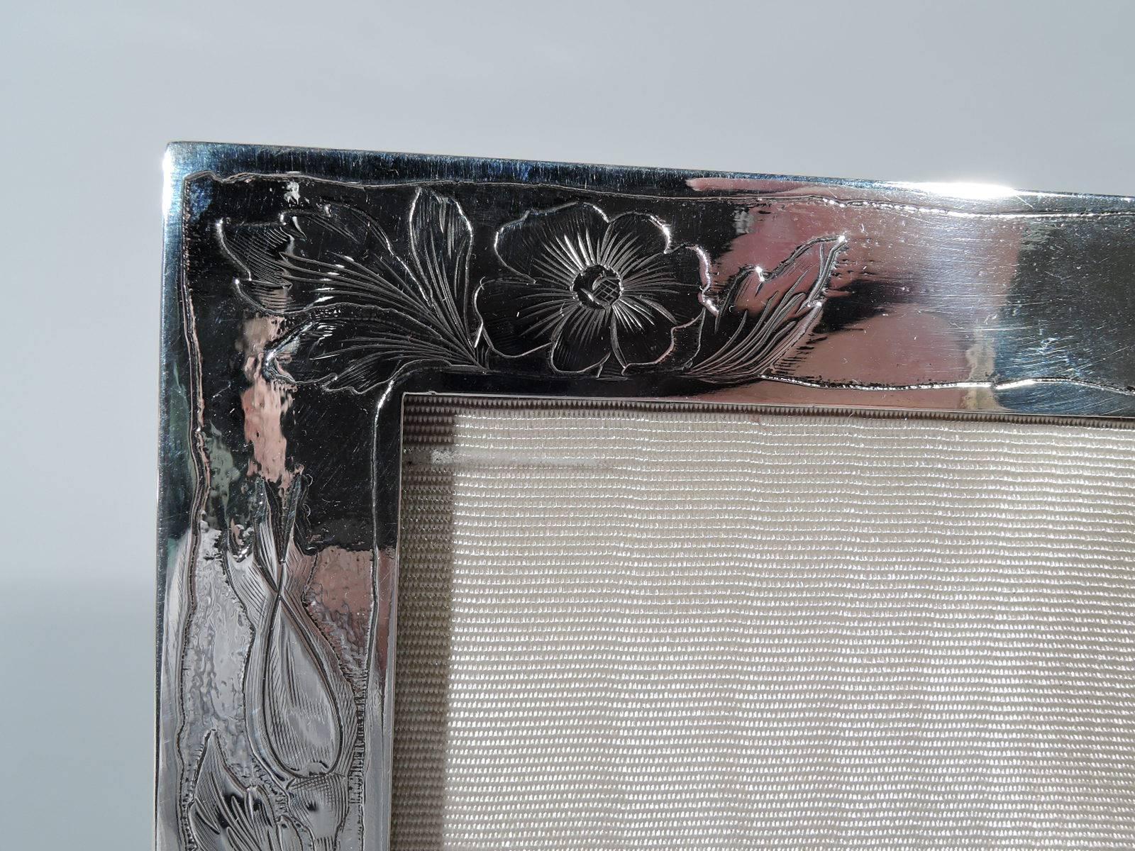 American Art Nouveau sterling silver picture frame. Rectangular window and flat acid-etched border with wrap round flowers and foliage between irregular borders. Top vacant. With glass, silk lining, and velvet back and hinged support. For portrait