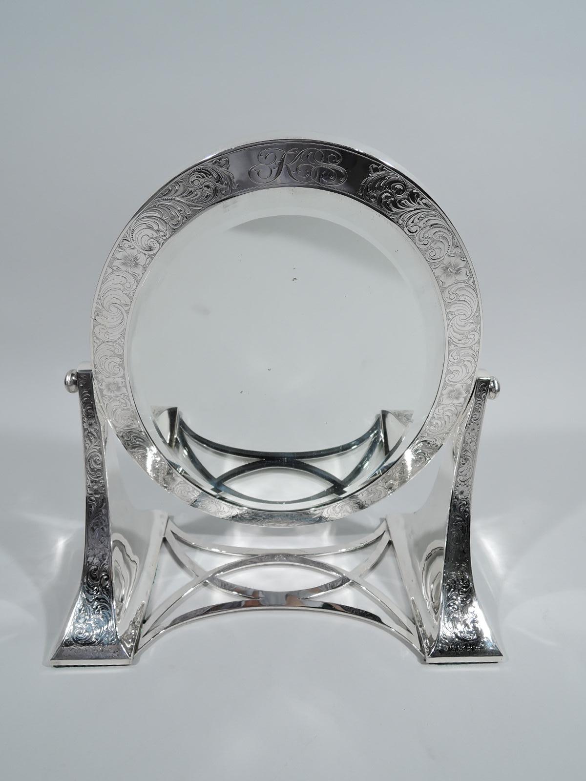 Turn-of-the-century Art Nouveau sterling silver mirror. Made by Lebkuecher in Newark. Two bracket supports joined by concave and crisscrossing stretchers. Hinged swing oval frame inset with beveled glass. Dense and fluid engraved scrolls, leaves,