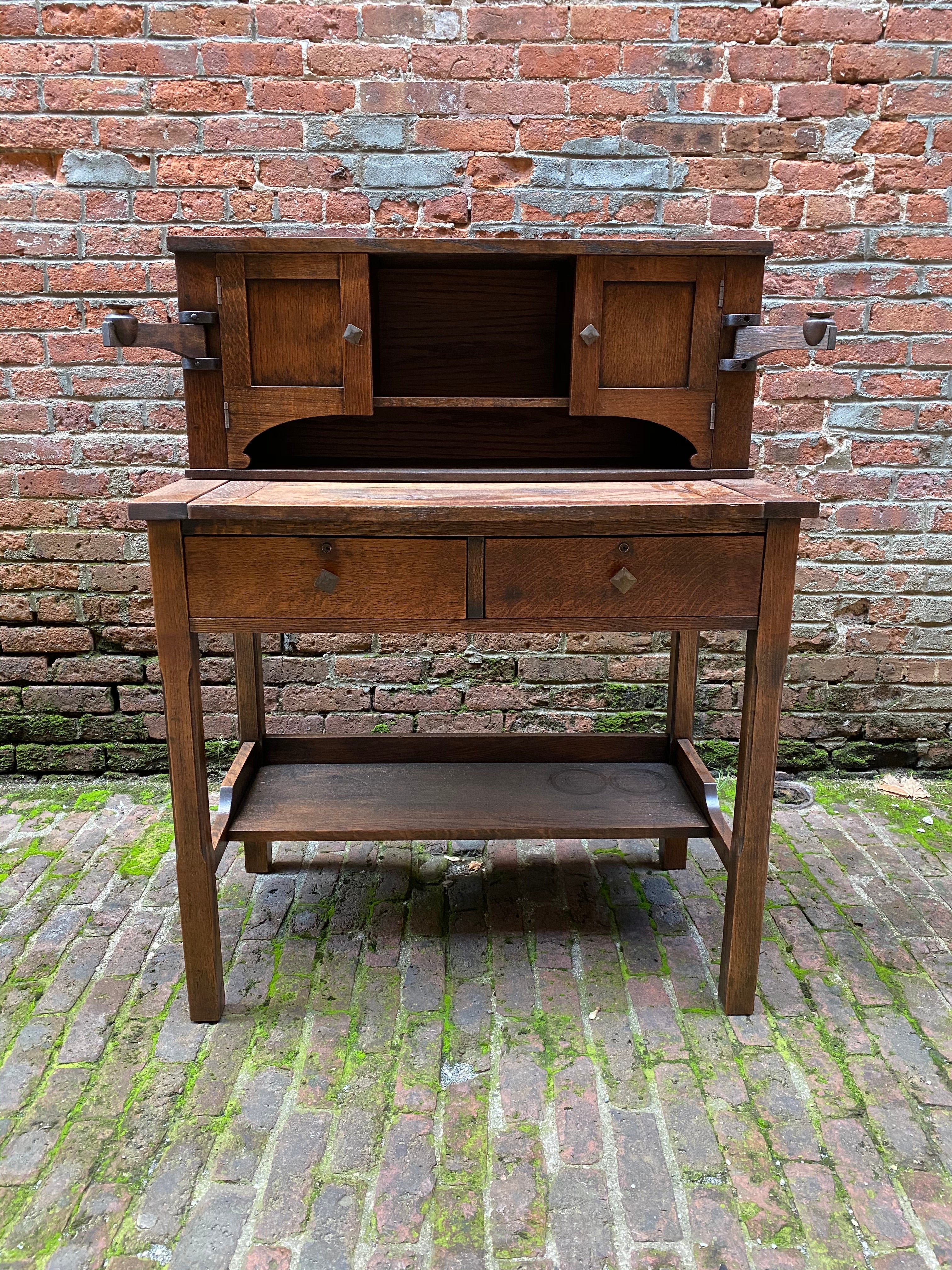 American oak Arts & Crafts writing desk. Featuring solid oak constuction, sliding work space, cubby holes, solid brass knobs, two drawers and articulated candleholder arms. Circa 1900-1910.

Structurally sound and sturdy construction. Marks on