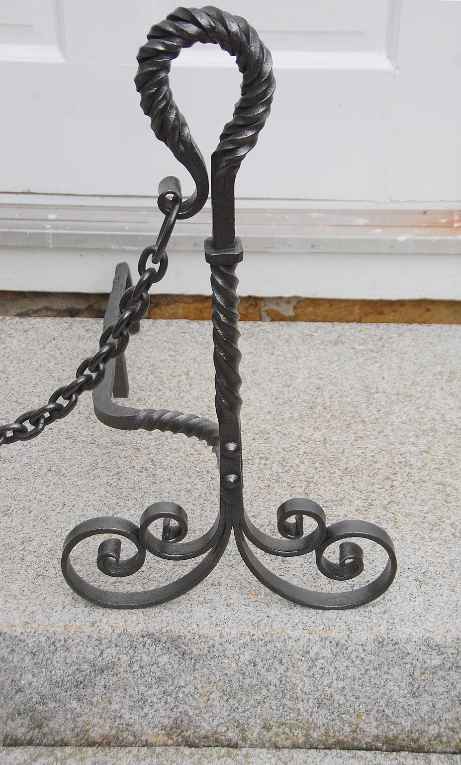 American Arts and Crafts Period wrought iron pair of andions. These 24 1/2 inch high hand wrought andirons have twist loop tops and hand split iron scrolling base. Complete with removable chain. Circa 1900.