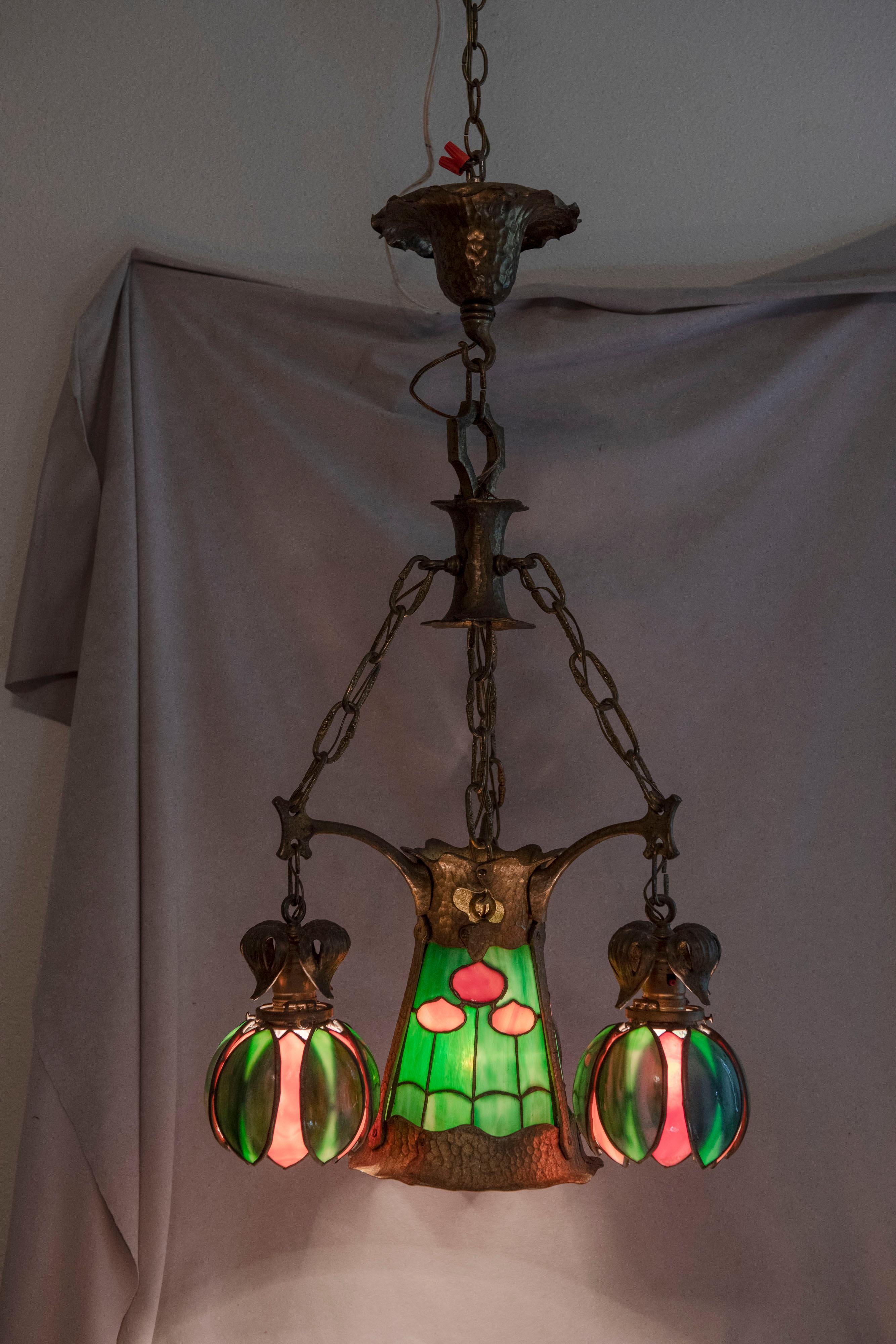 This colorful quality little chandelier offers good light and wonderful aesthetics. The center section has a pretty floral pattern of leaded glass. The 3 accompanying shades are all bent glass into a floral shape. All the glass is original and with