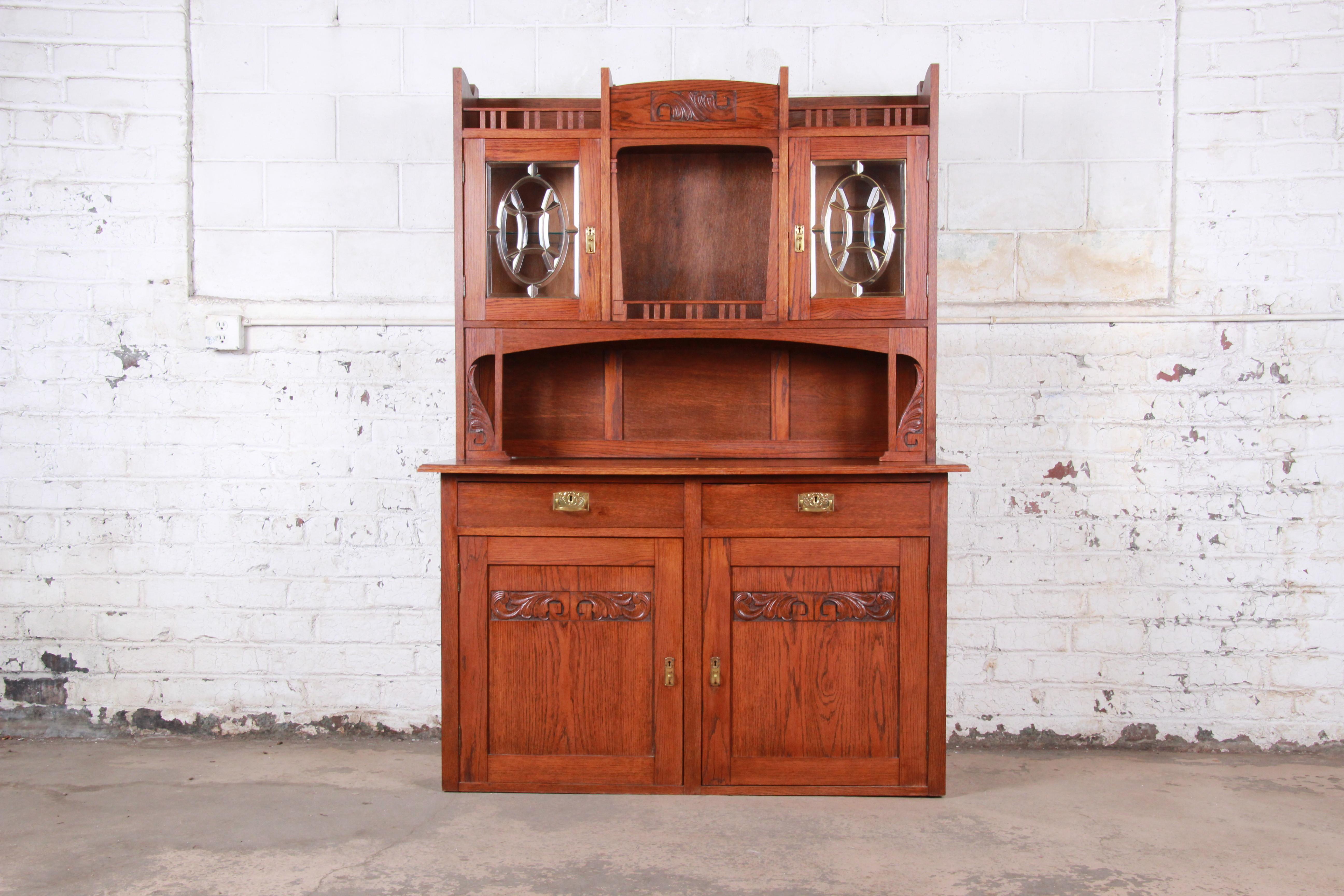 An exceptional Arts & Crafts carved oak bar cabinet or sideboard with hutch

USA, mid-20th century

Solid carved oak + beveled glass + brass hardware

Measures: 55