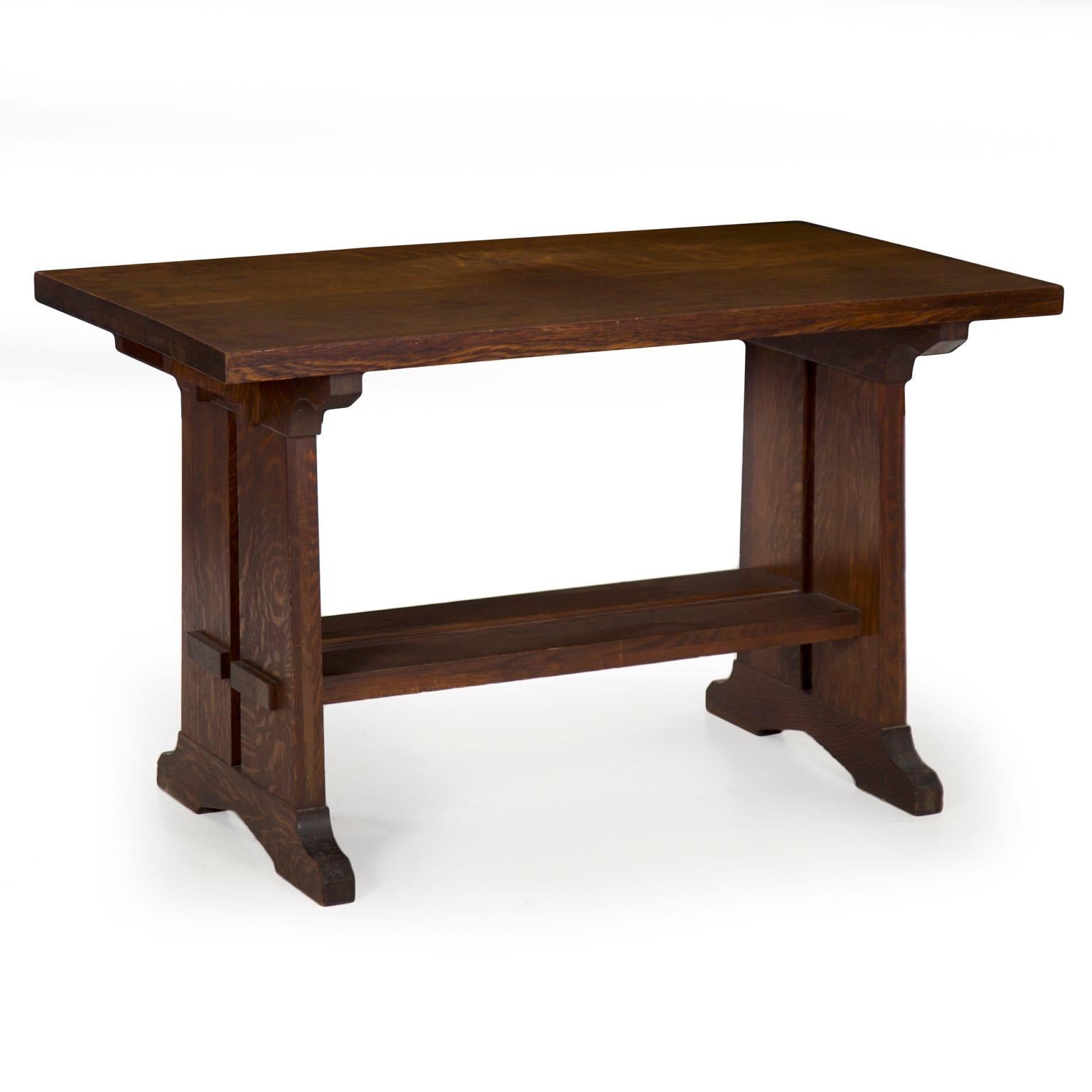 This angular writing table is an angular and austere product of the Arts & Crafts movement retaining an old finish that has oxidized nicely with time. The rectangular top is plain and unembellished, resting over scroll-cut capitals tenoned on thick