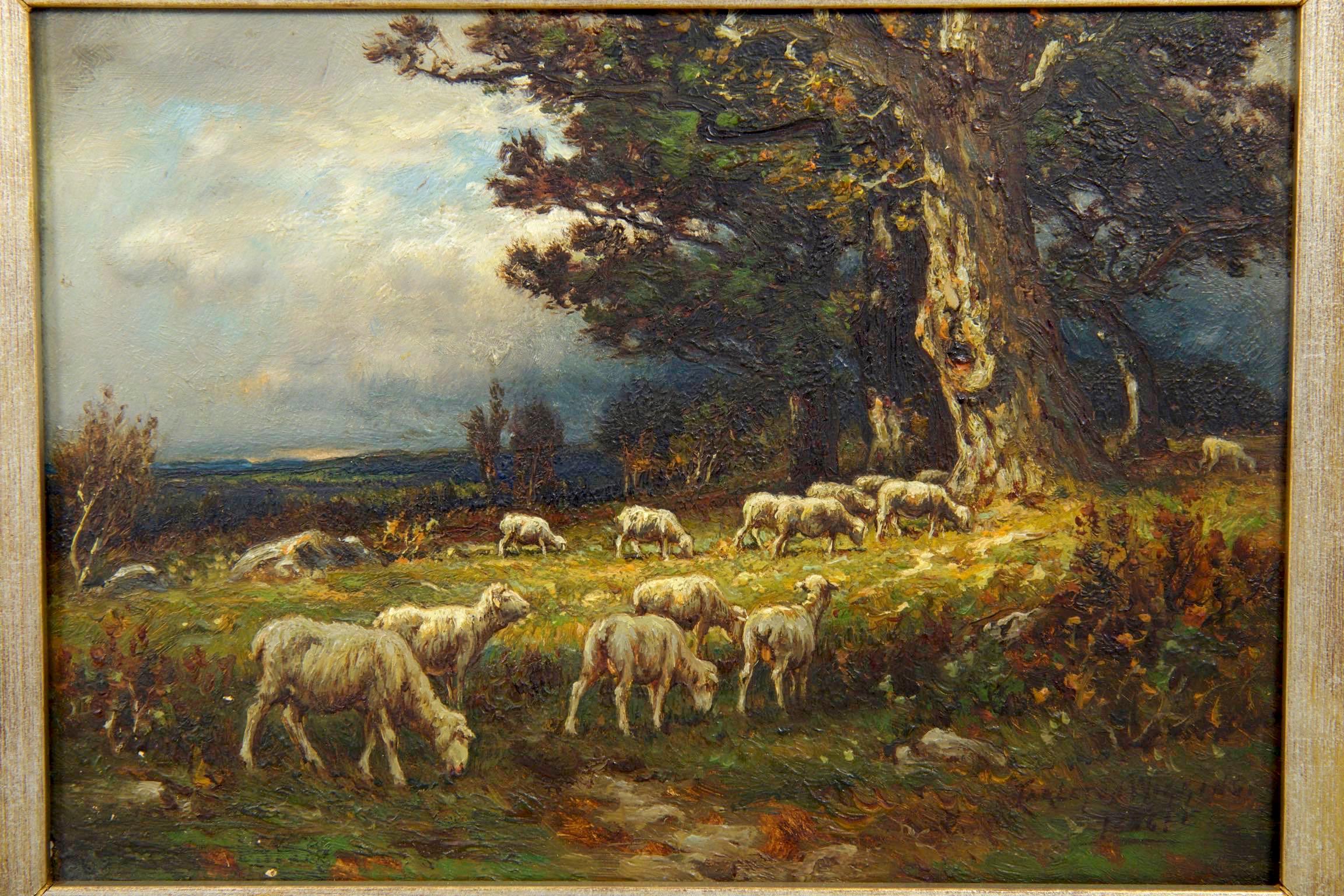 A small and very attractive Barbizon oil painting of a cluster of sheep wandering through a green pasture beneath large oak trees under cloudy skies, the scene is typical of Carleton Wiggins with a bleary impressionism that captures the scene and