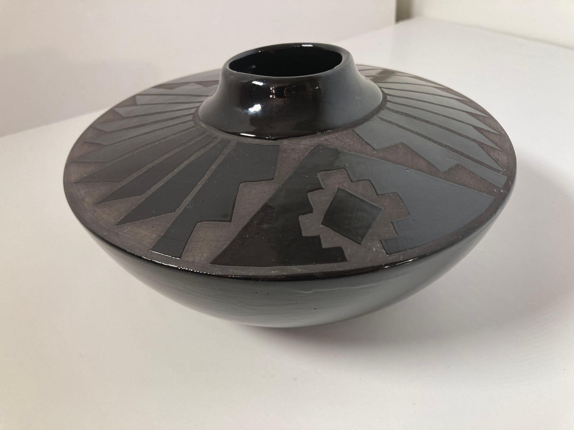 Mata Ortiz Stil schöne handgedrehte geometrische blackware Vase, schwarz auf schwarz.
Das runde Keramikstück ist aus schwarzem glasiertem Ton gefertigt und mit einem einzigartigen geometrischen Pfeildesign im Stil des Töpfers von Mata Ortiz