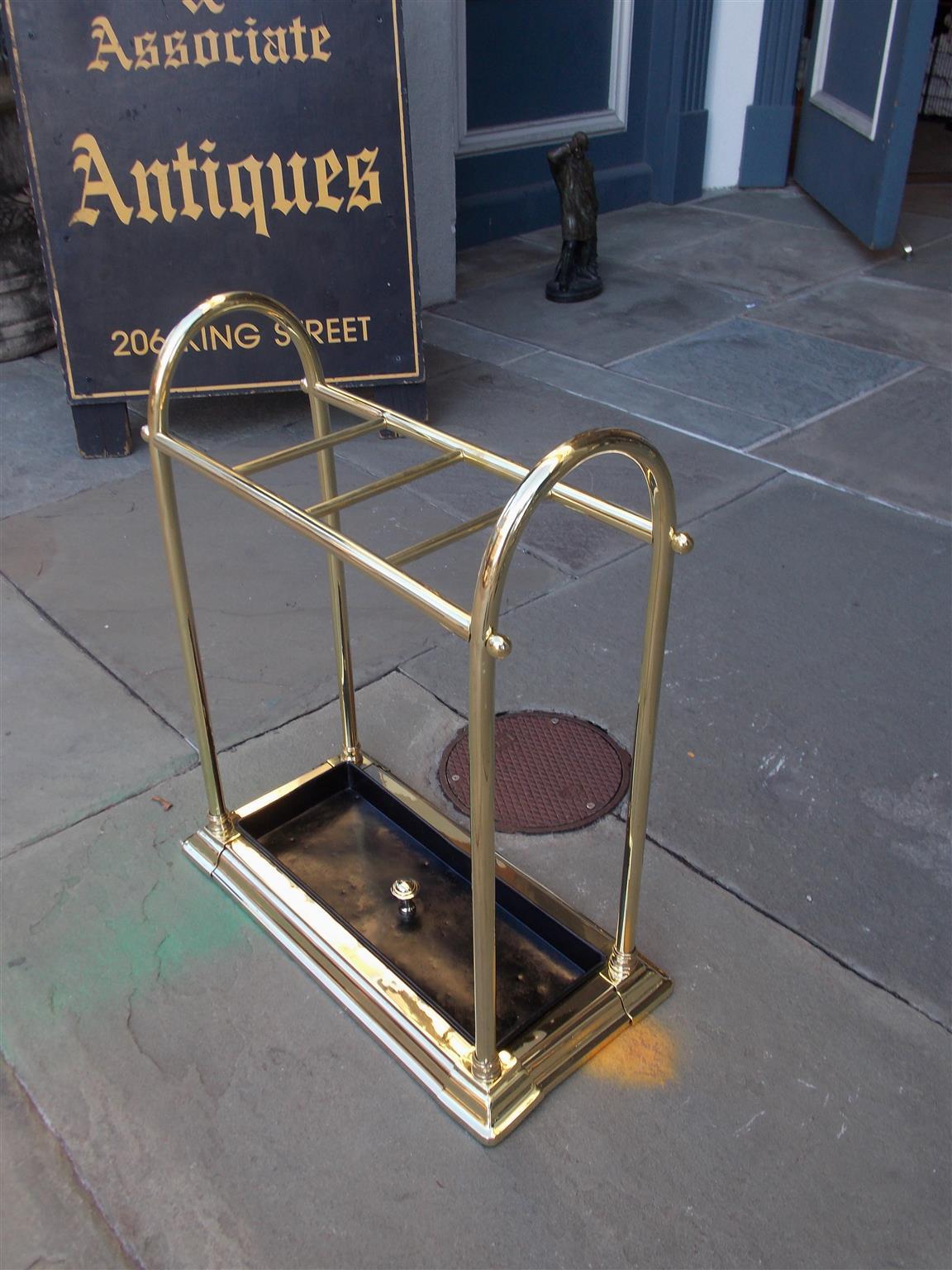 American brass and cast iron arched pole four slotted umbrella stand with removable brass knob pan and resting on a molded edge base, Late 19th century.