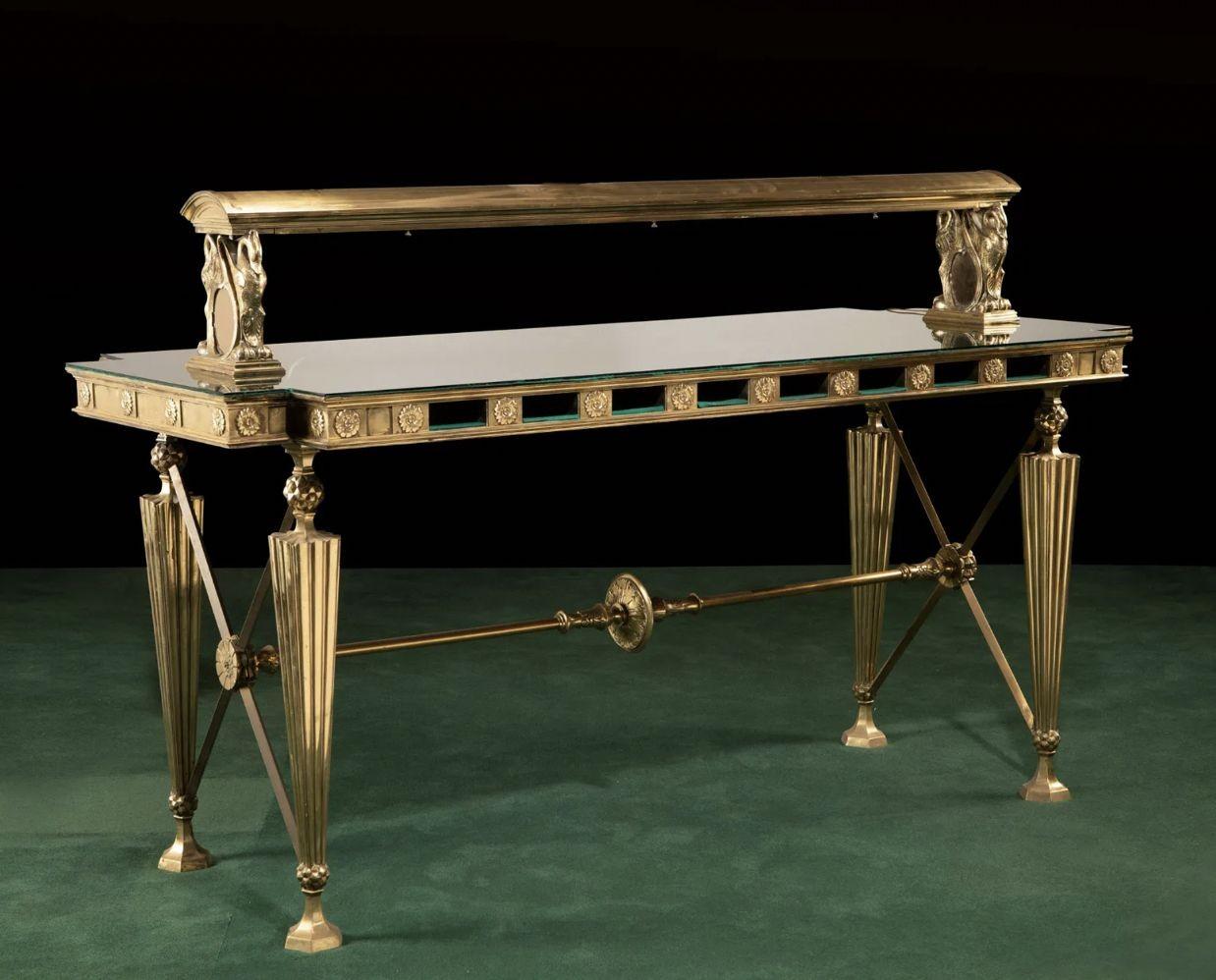 An American bronze and glass banking table
Early 19th century
Each Greco-Roman-style, the table with a rectangular notched-corner top with a medallion designed apron, four legs, cross members at each end, and a central support with center roundel,