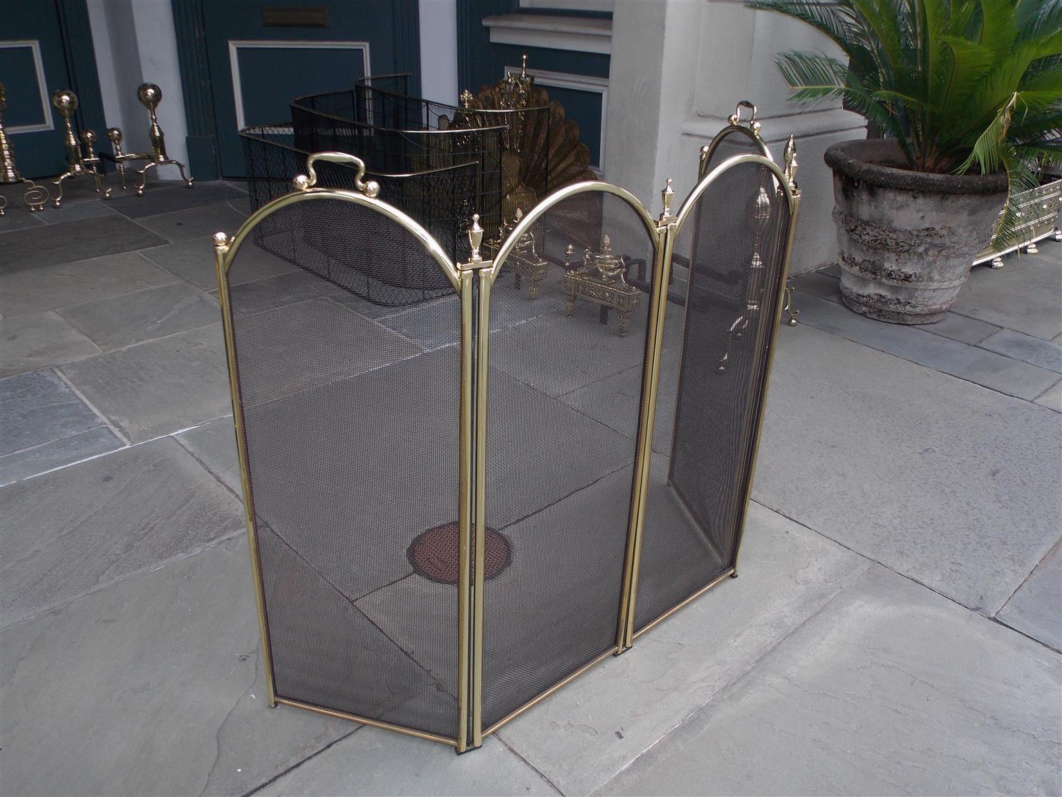 American brass and wire folding four panel arched fireplace screen with flanking side handles and urn finials, Late 19th century.