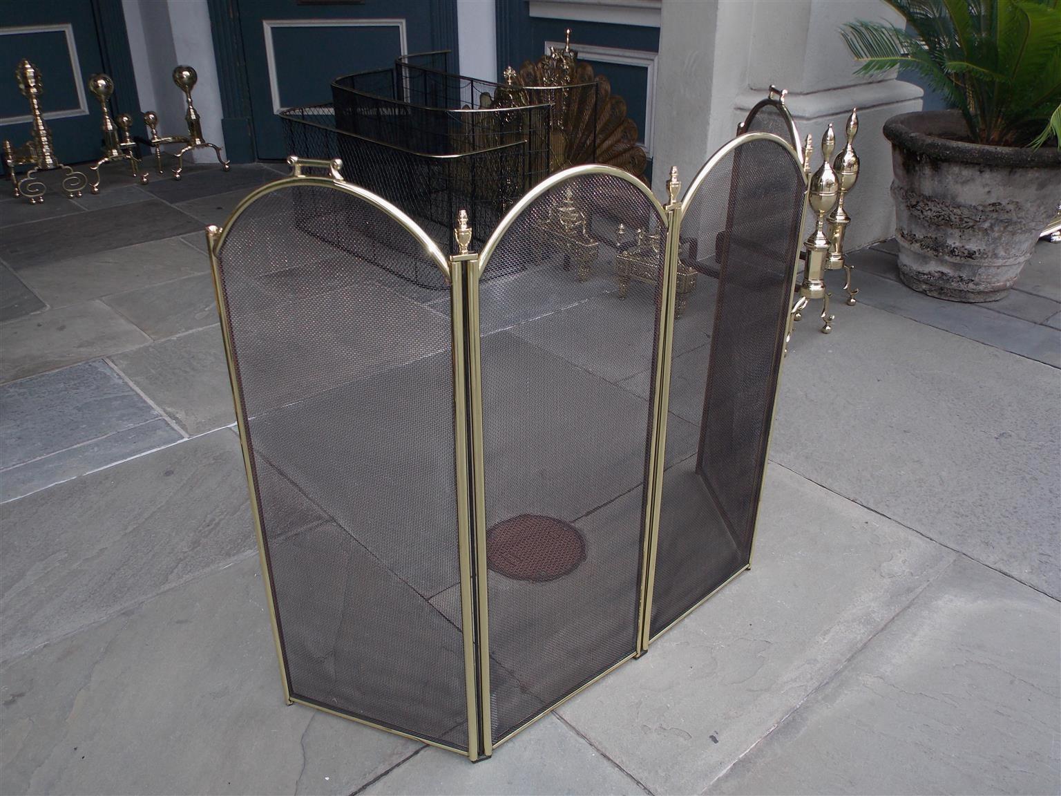 American brass and wire folding four-panel arched fireplace screen with flanking side handles and urn finials, Late 19th century.
