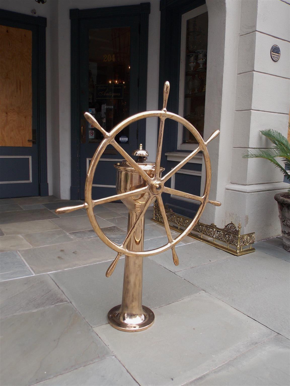 American brass nautical ship wheel with a centered brass hub connecting seven spindles with bulbous handles, and mounted to a solid brass geared pedestal with circular base and four exterior mounting holes, Mid-19th century. Stamped by maker: Neafie