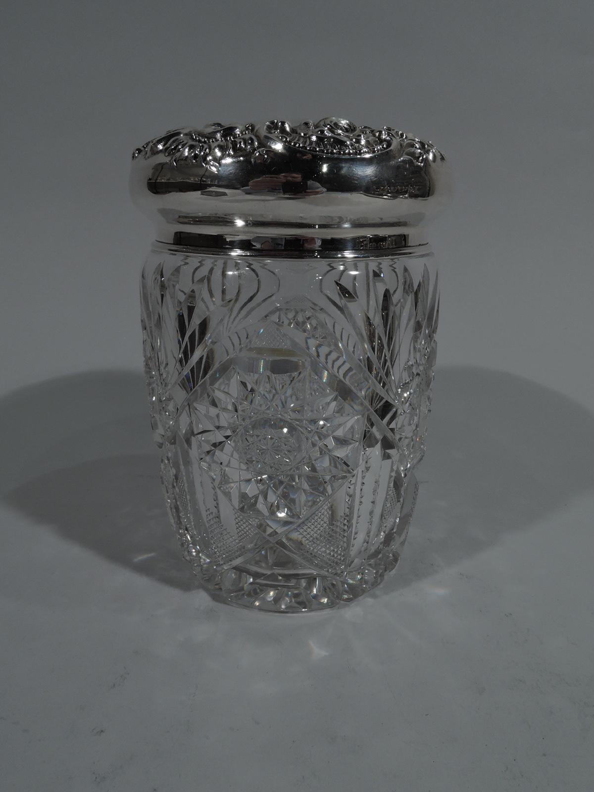 American brilliant-cut glass jar with sterling silver cover. Cylindrical with fans, stars, diaper, and facets. Cover curved with vacant centre bordered by repousse flowers and scrolls. Cover marked including stamp for Hamilton & Diesinger, a
