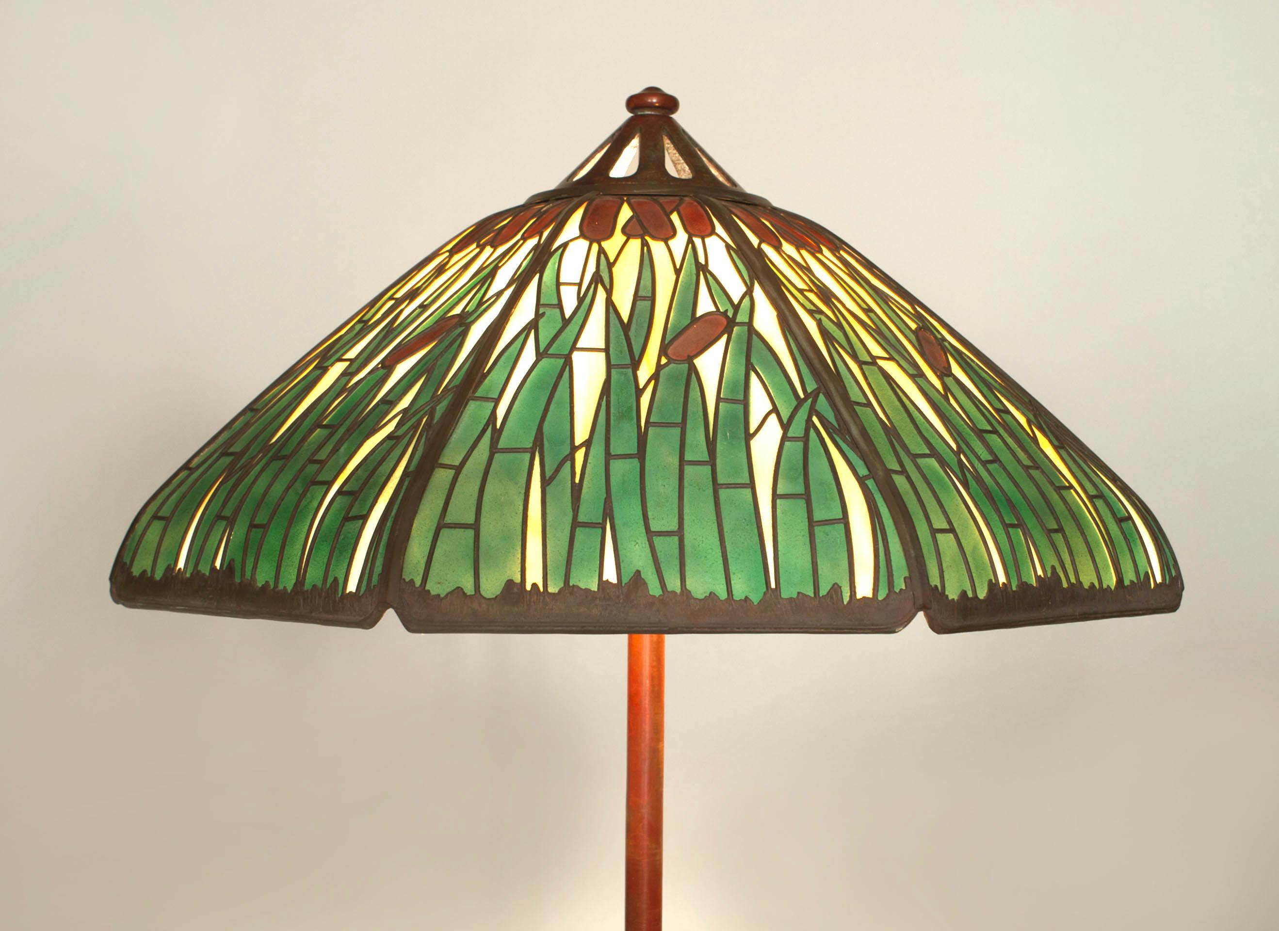 American Mission bronze adjustable floor lamp having 3 supports resting on a shaped base holding an 8 sided stained glass shade with cattail design. (signed: HANDEL)
