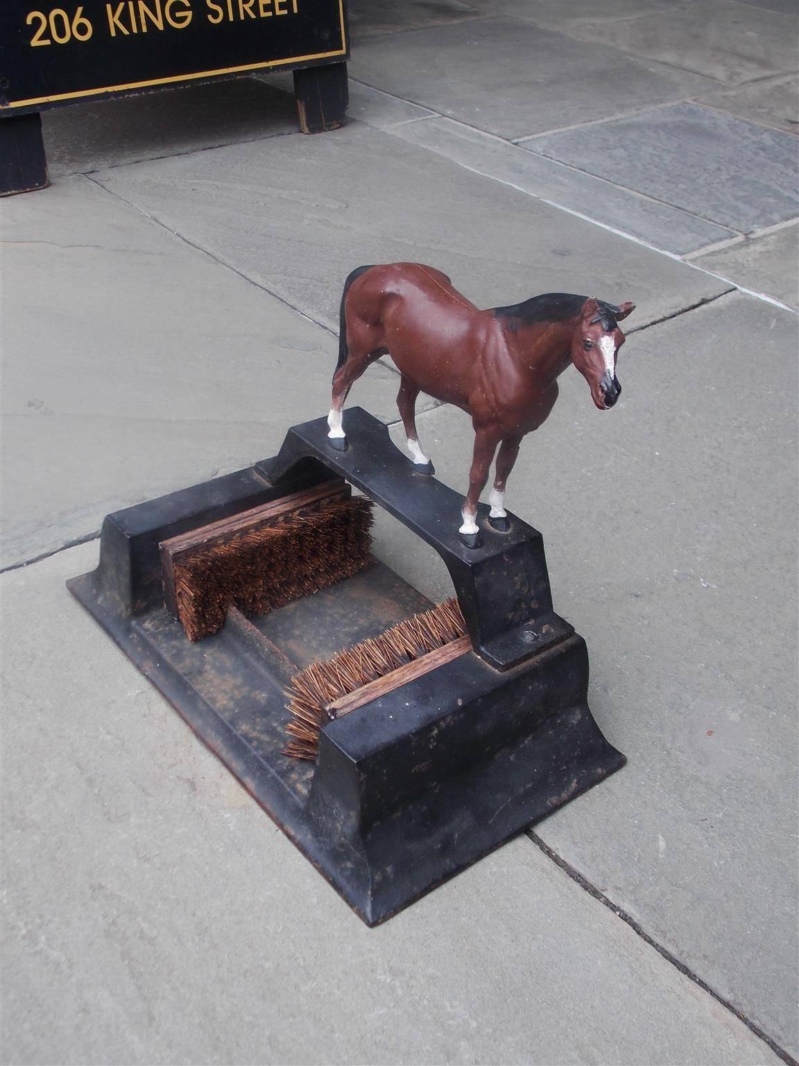 American cast iron boot scraper with centered perched horse, supporting plinth columns with flanking wood brushes, and resting on a molded edge rectangular base. Mid-19th century.