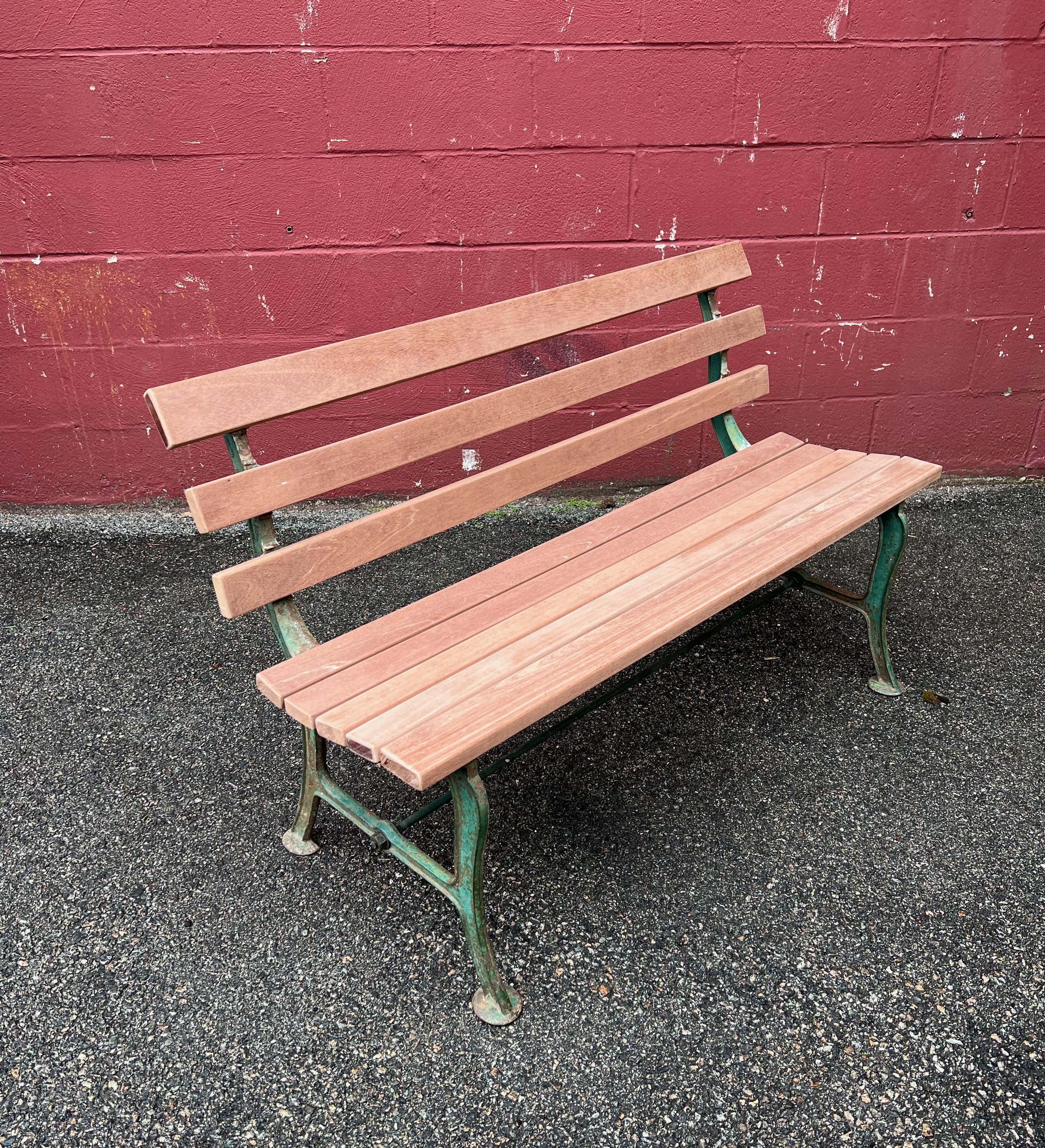 This late 19th or early 20th century park bench is a beautiful and historic piece of outdoor furniture. The cast iron base, with its original paint, adds character and charm to the bench, while the recently replaced untreated mahogany slats ensure