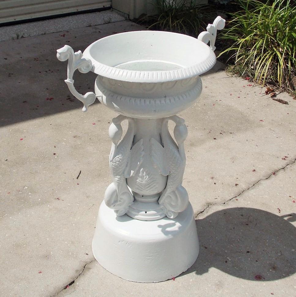 American cast iron and powder-coated campana garden urn with a molded edge top, decorative scrolled floral and medallion relief, flanking scrolled foliage side handles, centered perched swans, and resting on a circular plinth base, Mid-19th century.