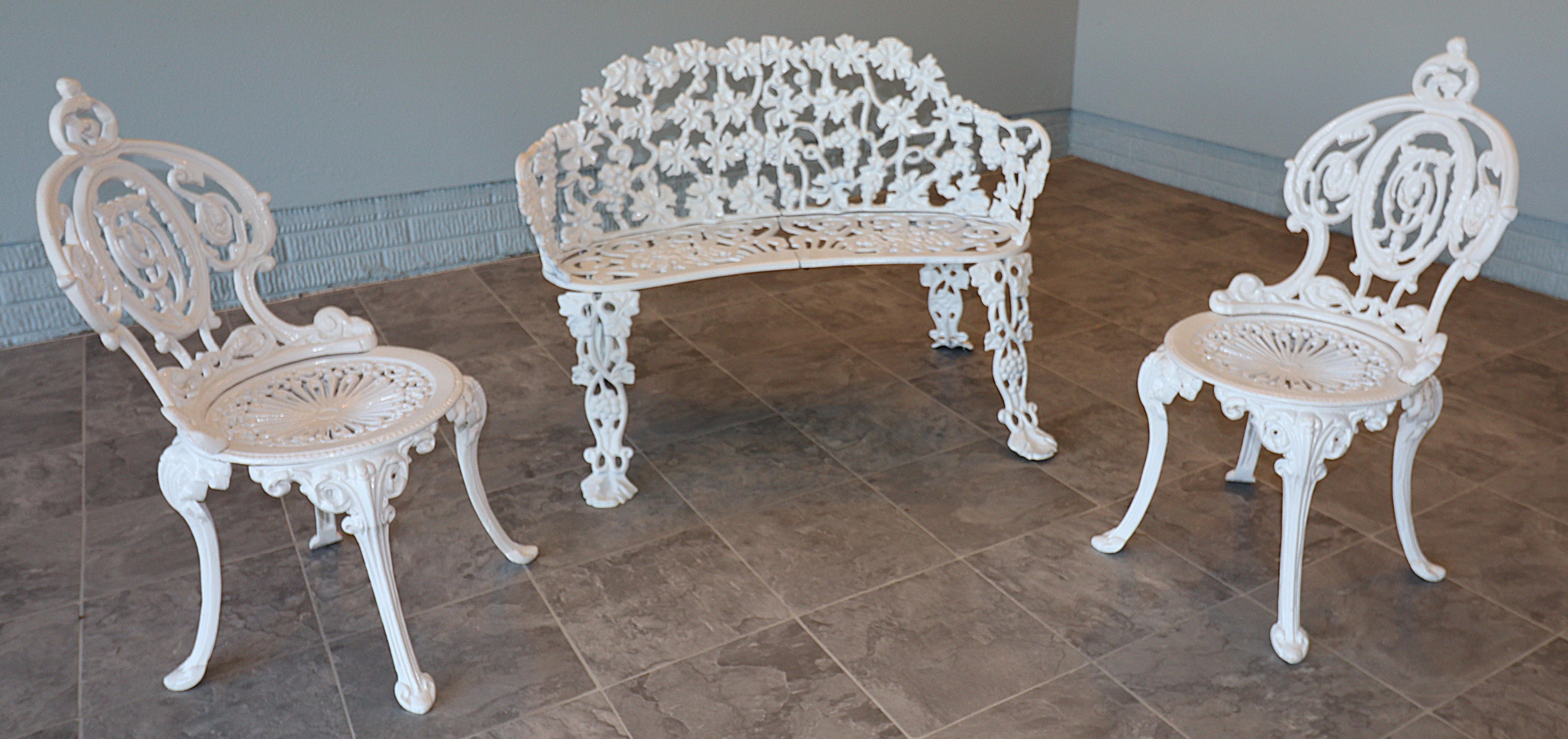 An elegant three-piece Victorian Revival garden suite comprising two cast iron side chairs and a cast iron, two-seat grapevine settee, circa 1930s–1950s. The side chairs retain their foundry stamps beneath the seats, affirming provenance from the