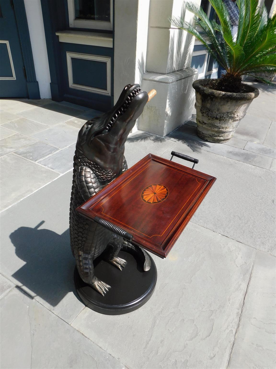 American cast resin standing alligator with a verdigris finish, mounted cigar in teeth, arms holding rectangular satinwood inlaid tray with handles, and resting on a circular painted molded edge base, 20th century.
36