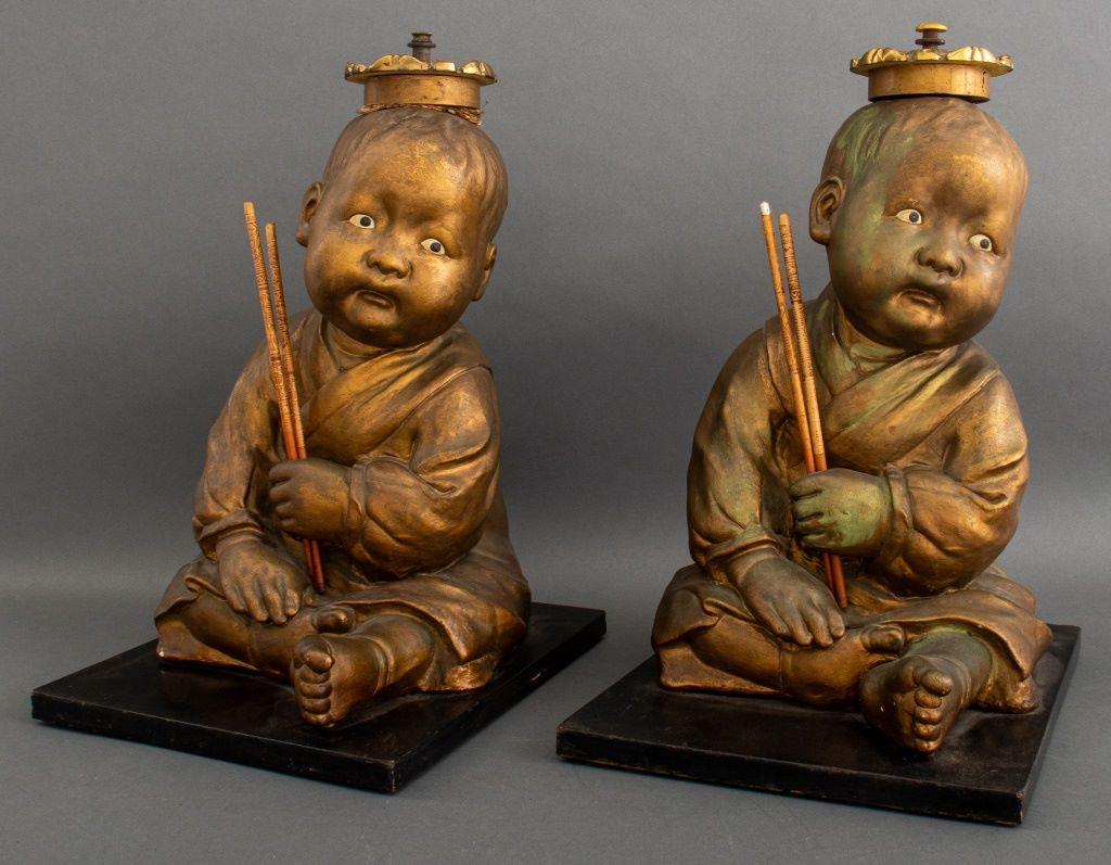 Pair of American Chalkware Chinoiserie Seated Infant 3D figurative plaster sculptures painted gold on black wood bases, apparently unmarked.