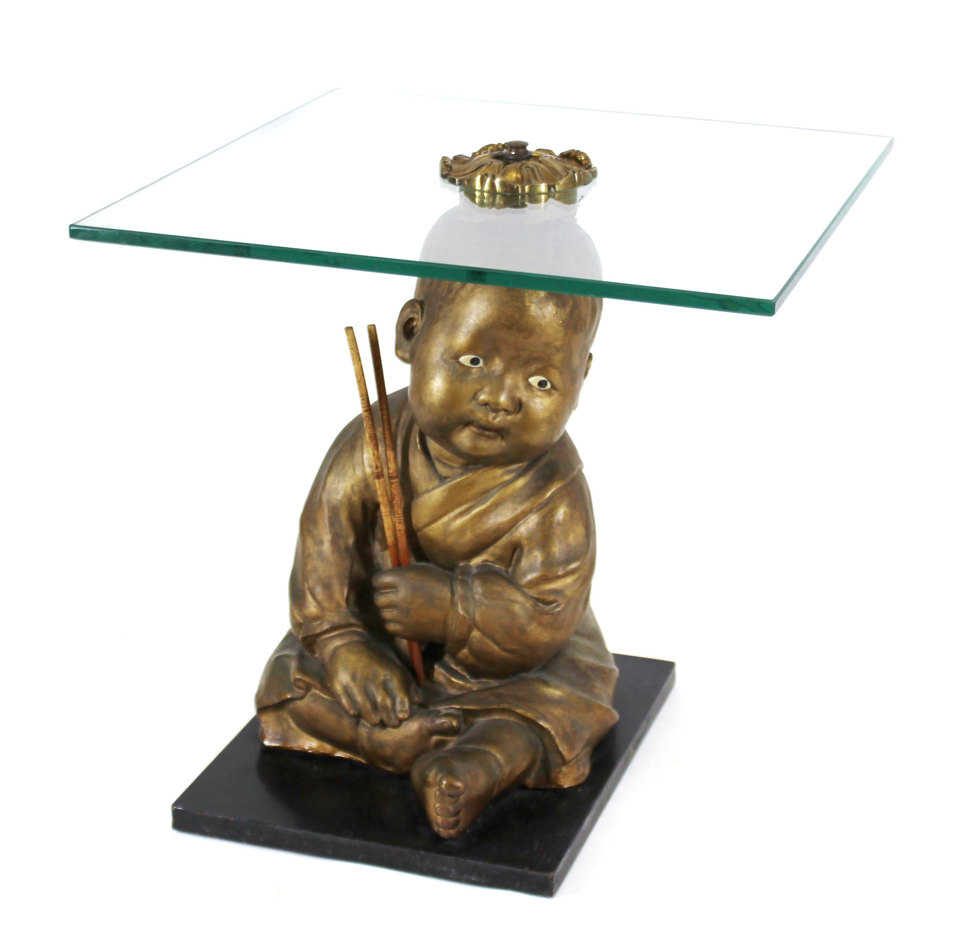 American chalk ware figures depicting gold painted seated Asian infants holding chopsticks, turned into a pair of side tables with square cut glass tops.