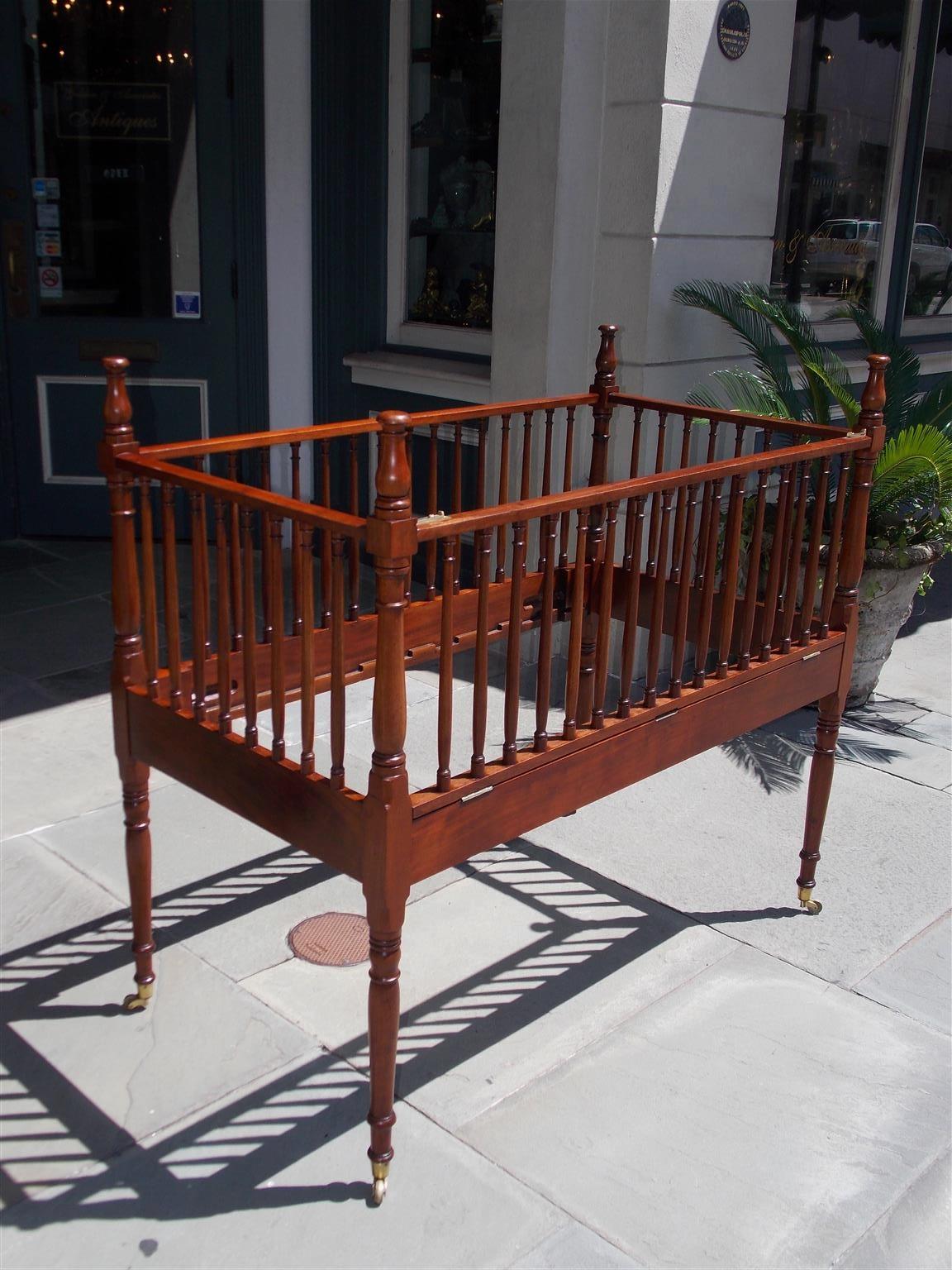 American Charleston Mahogany child's crib with flanking side and end rails, turned bulbous ringed spindles with finials, single triple hinged folding side rail, corner bed bolt fasteners with interior fitted notches for splats, and terminating on