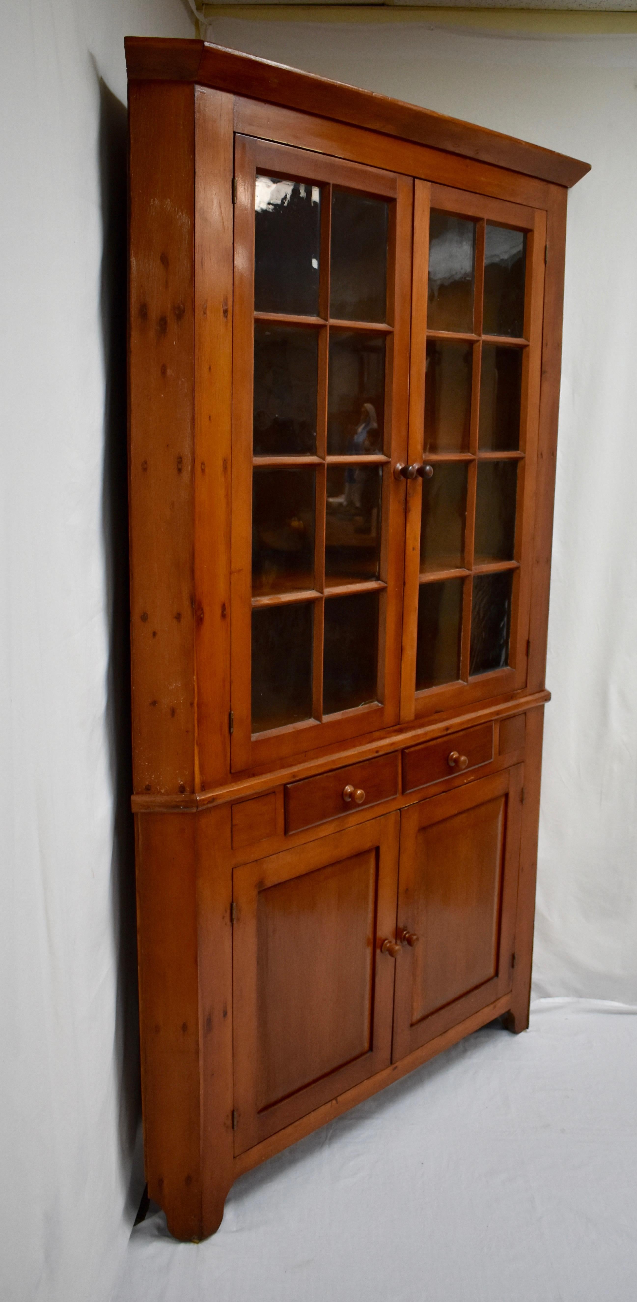Built in two pieces, this imposing late 19th century cherrywood corner cupboard from Maryland affords spacious storage and display using only 35” each side of a corner. The upper section has a plain crown and two wide-swinging doors, each with eight