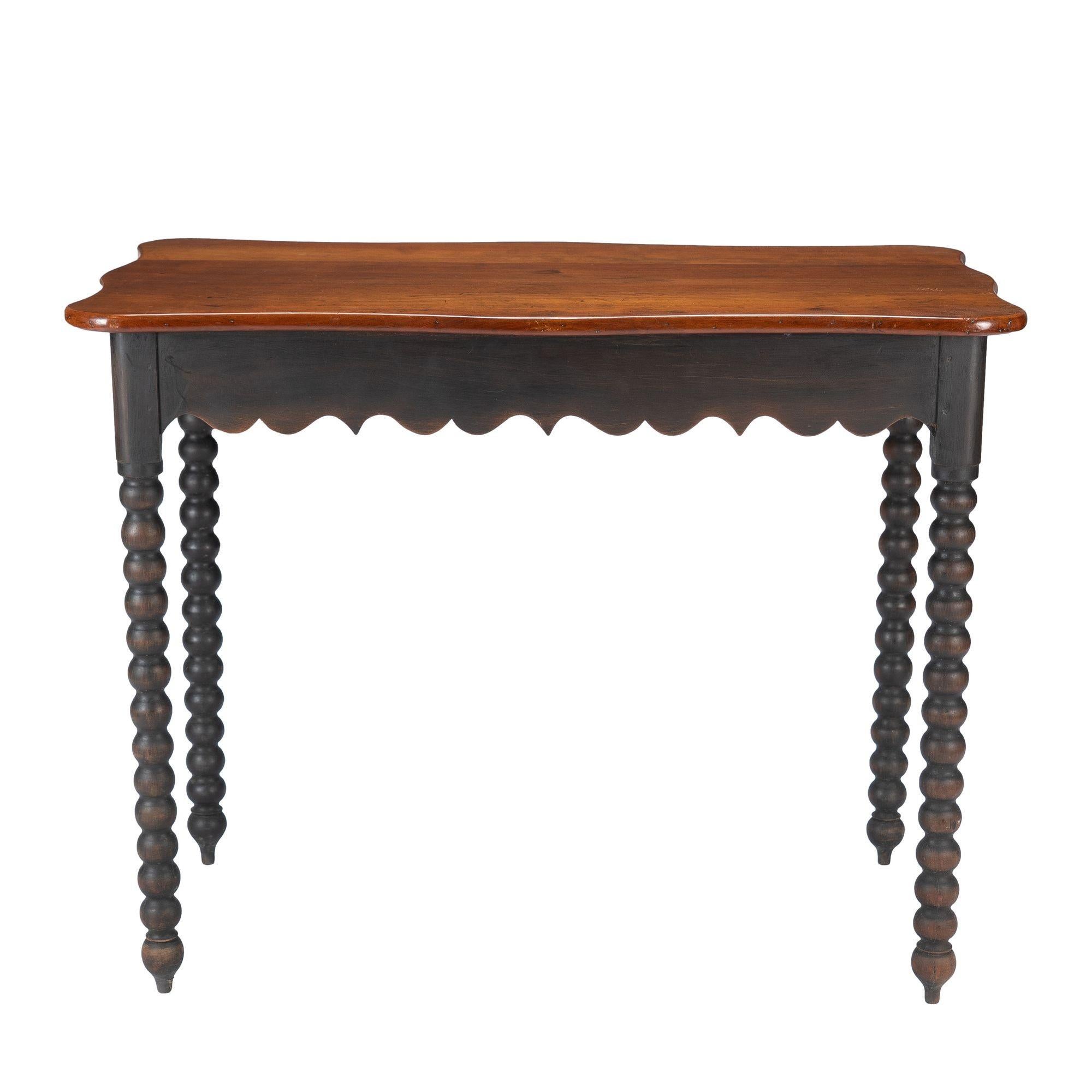 Rectangular work table a with shaped cherry wood top, an ebonized cherry scollop cut apron frame, and spool turned ebonized legs.
American, circa 1835.