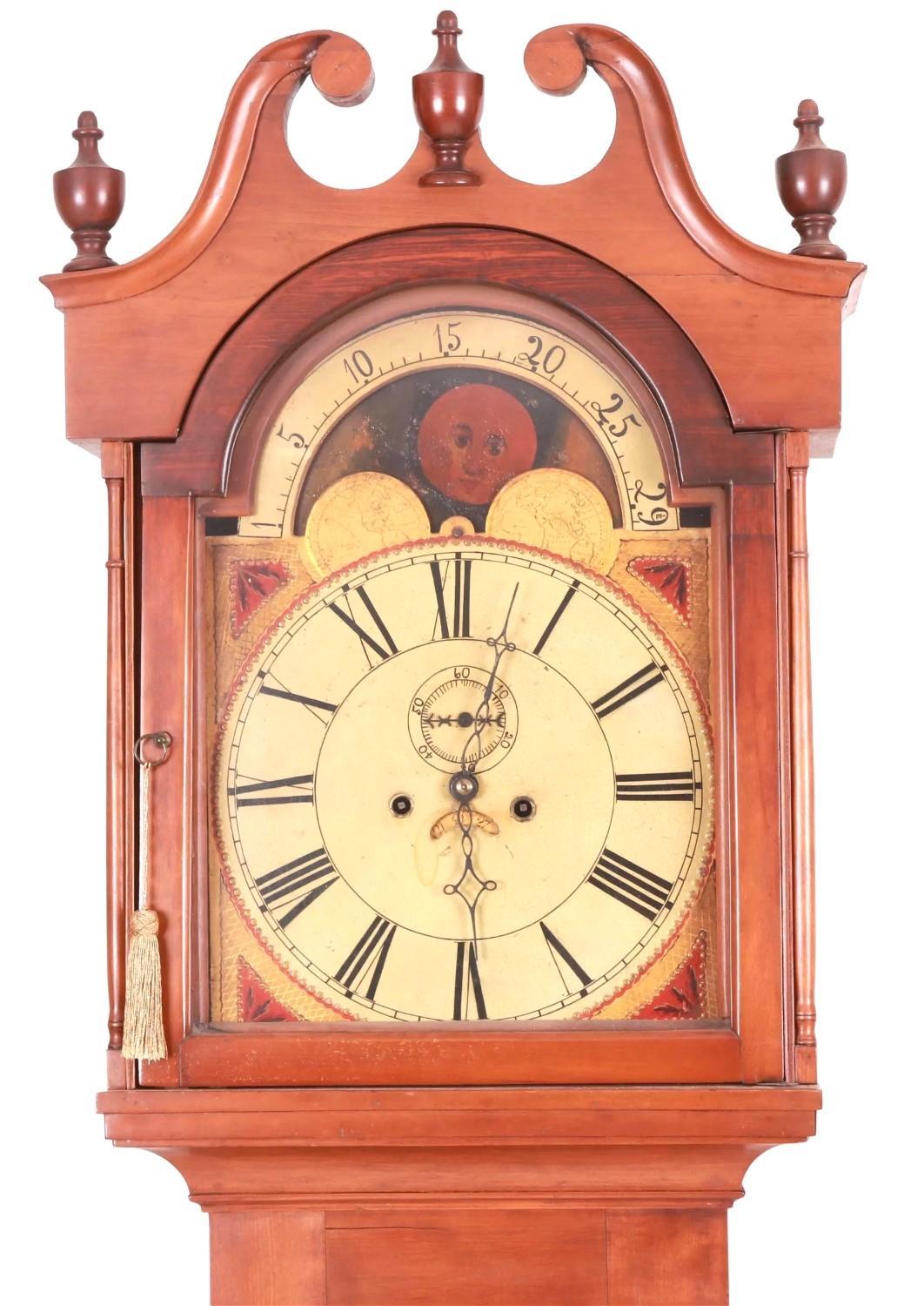 An early 19th century American tall-case clock with brass 8-day movement, the face having a moon-phase dial painted with ships and other scenes. The cherrywood case having cove moldings at the base, chamfered corners with lamb's tongue terminals, a