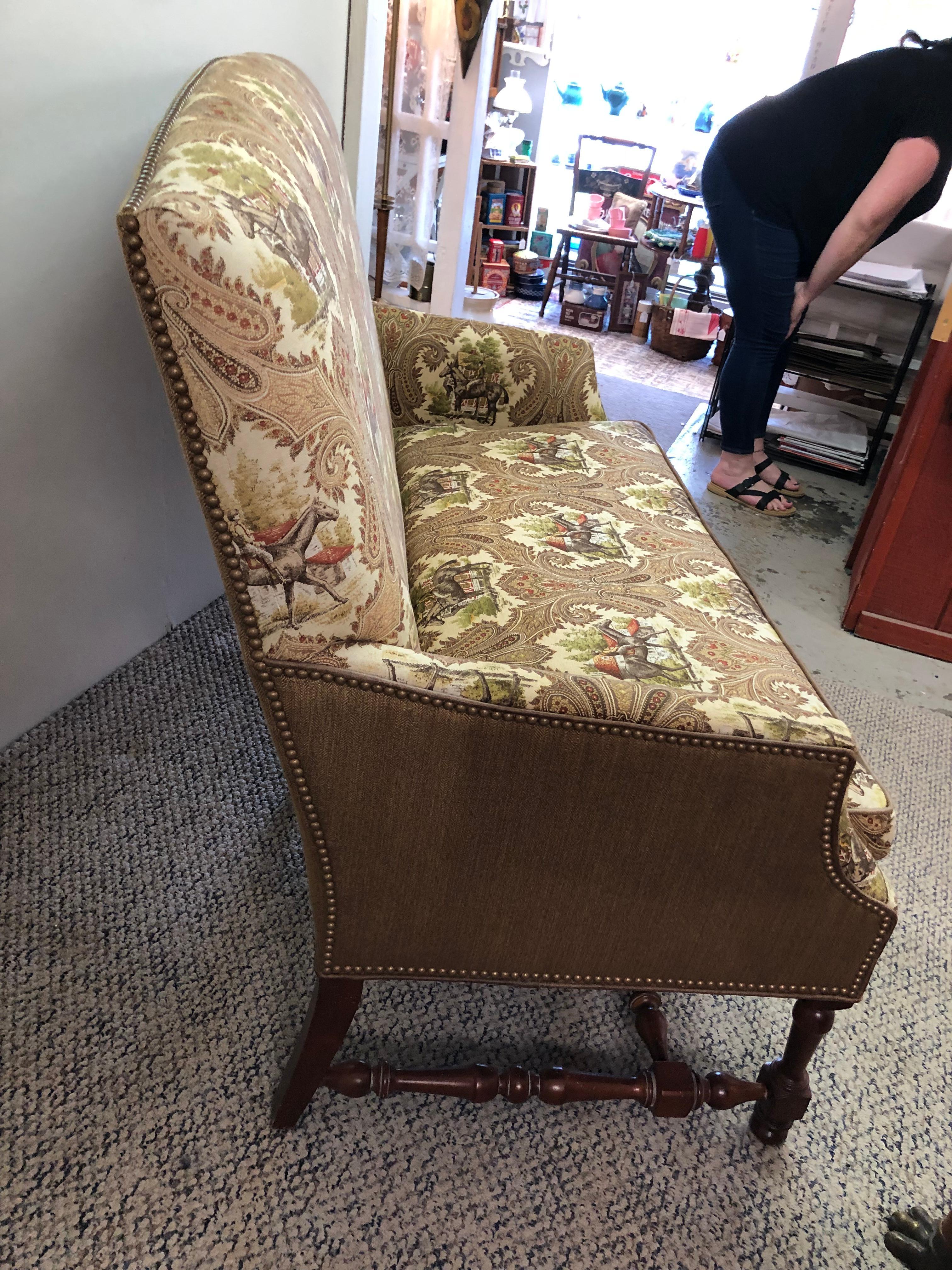 A stylish equestrian motif upholstered settee loveseat having turned walnut base, high back, Ralph Lauren-esque horsey fabric in earth colors with coordinating tweed and brass nailheads on the back. Great looking from every angle and comfortable.