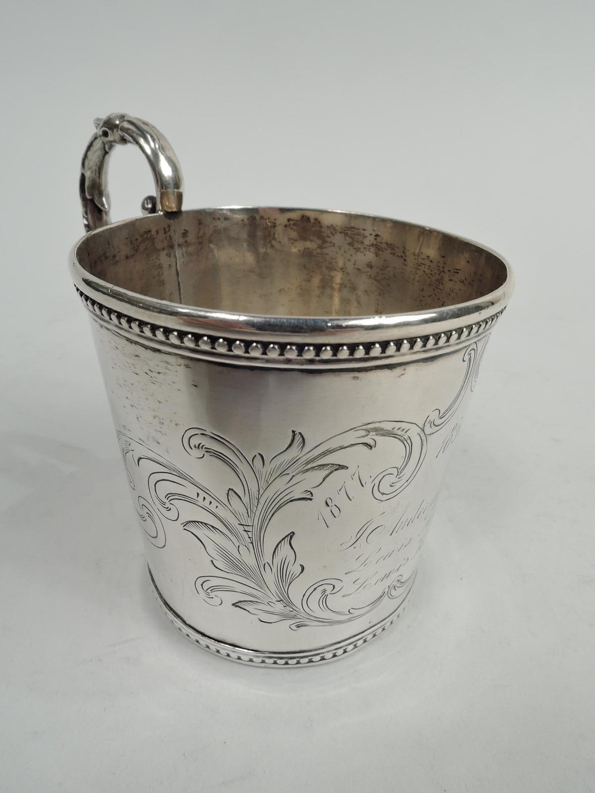 Classical coin silver christening mug. Made by Tifft & Whiting in North Attleboro, Mass., ca 1850. Straight and tapering sides with beaded rims. Three names and 3 birthyears (1851, 1877, and 1908) engraved in leafing scrolled frame. Leaf-capped