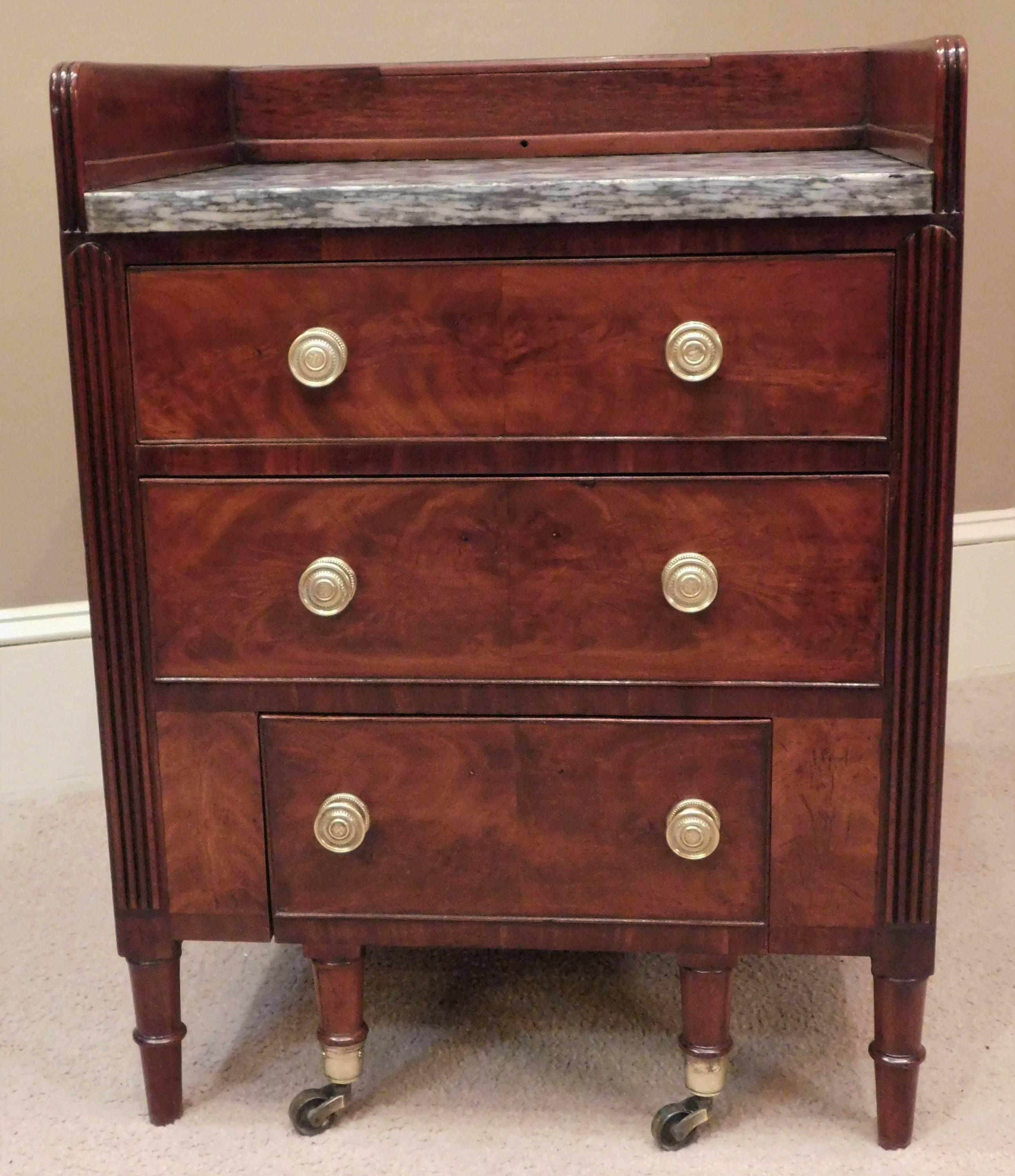 This wash stand and commode has its original French polished mahogany and figured mahogany veneer with poplar secondary wood, removable King of Prussia marble top, old replaced brass pulls, and original castors and potty. Raised reeded gallery with