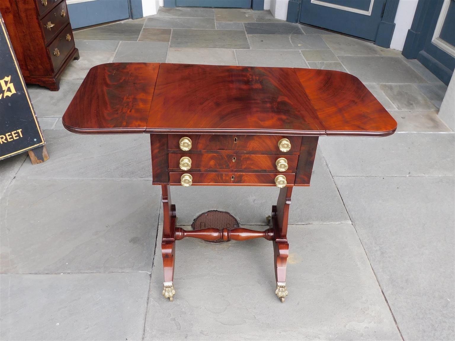 Table à trois tiroirs en acajou figuré de style classique américain, avec un bureau supérieur à l'intérieur aménagé, avec des cuivres à feuillage d'origine et des écussons centraux, des supports en lyre flanqués d'un brancard à bulbe, et reposant