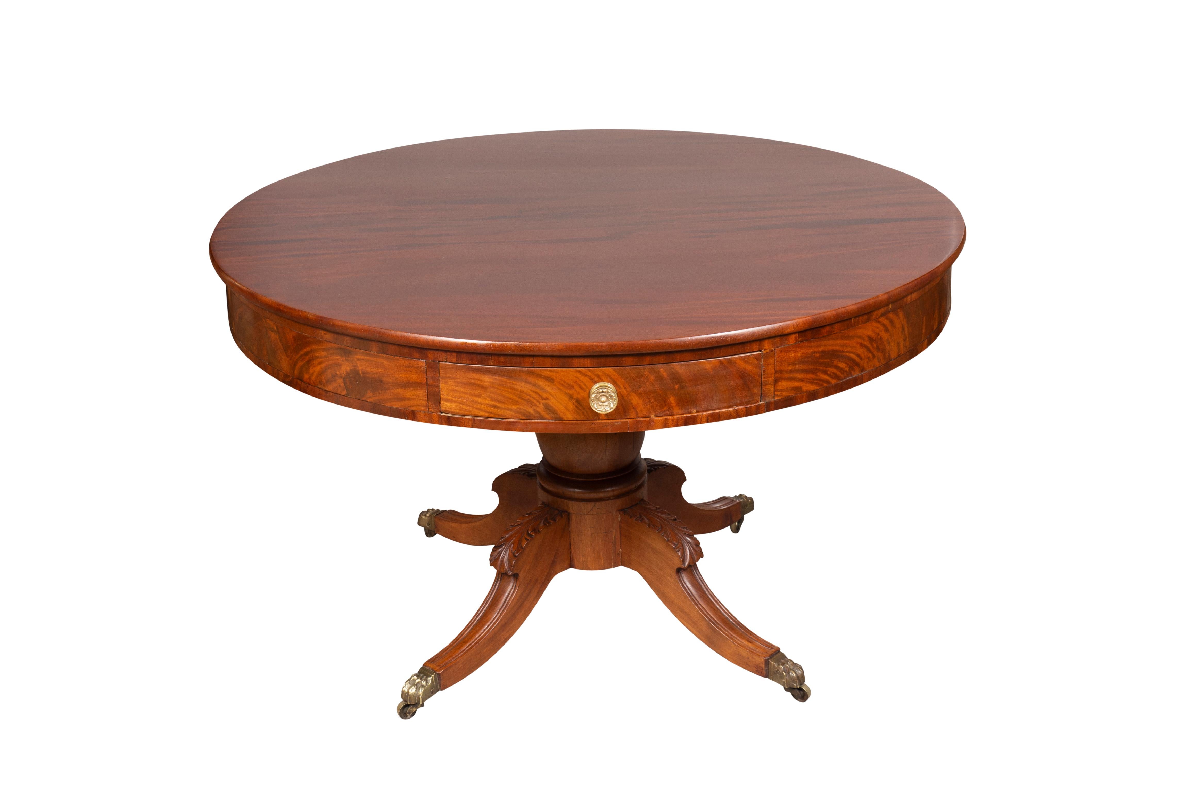 Likely Mid Atlantic states. With circular wood top with a conforming frieze with figured mahogany and with drawers with brass knob handles. Raised on a bulbous turned support joined by four carved saber legs and ending on brass paw cup casters.