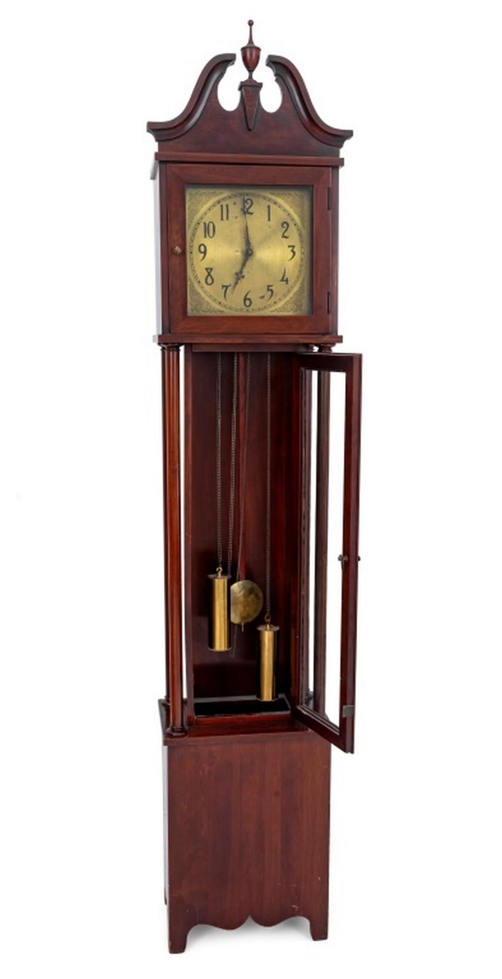 American Colonial Manufacturing Company Mahogany Tall Case Clock, with urn finial crest, gilt metal clock face with angel and floral decoration, having pendulum and two weights, the case having four carved columns above rectangular base with carved