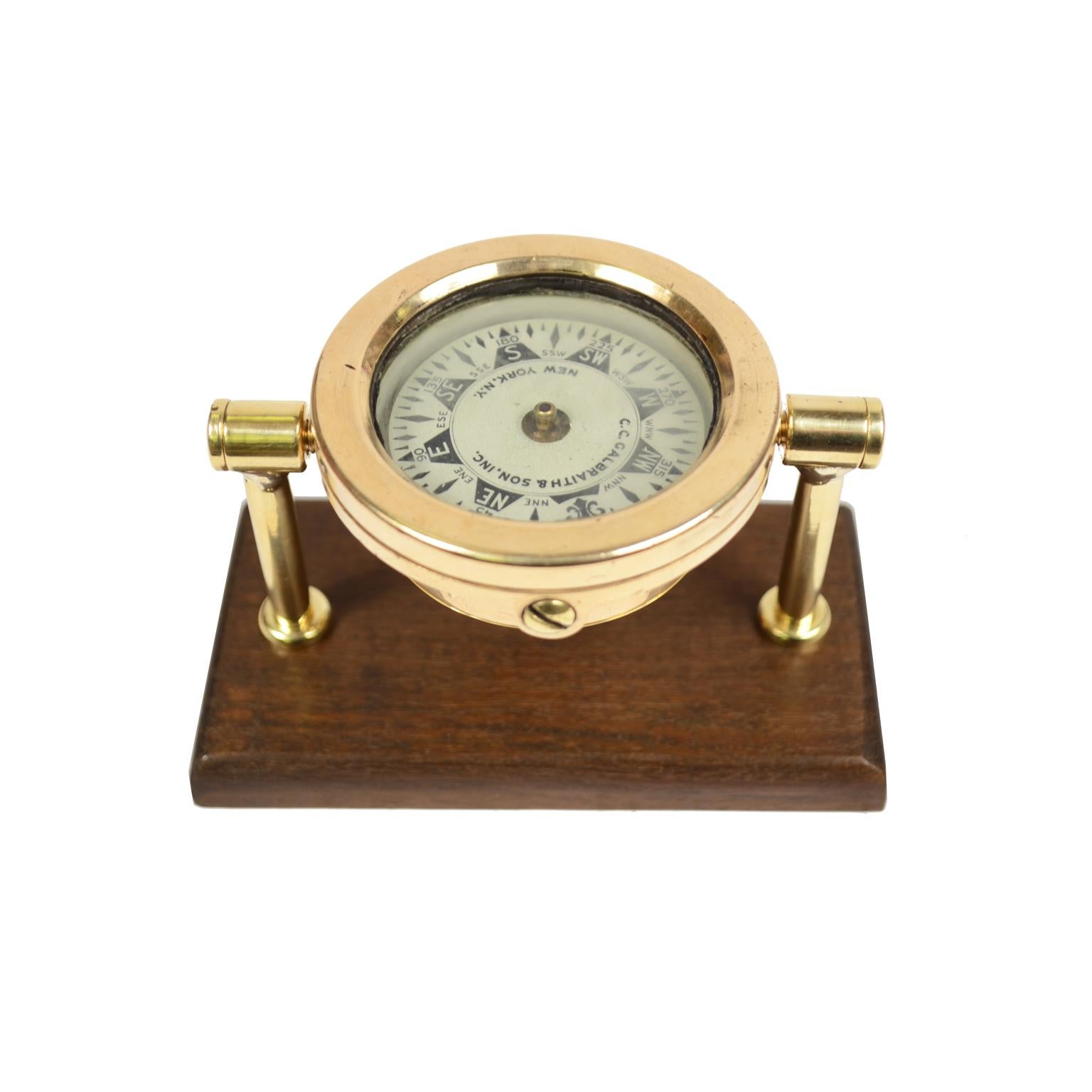 Small liquid compass on universal joint signed C.C. GALBRAITH & SON INC NEW YORK N.Y. from the early 1900s, mounted on a walnut board. The compass consists of a cylindrical box made of brass and bronze, on the bottom of which a hard metal stem is