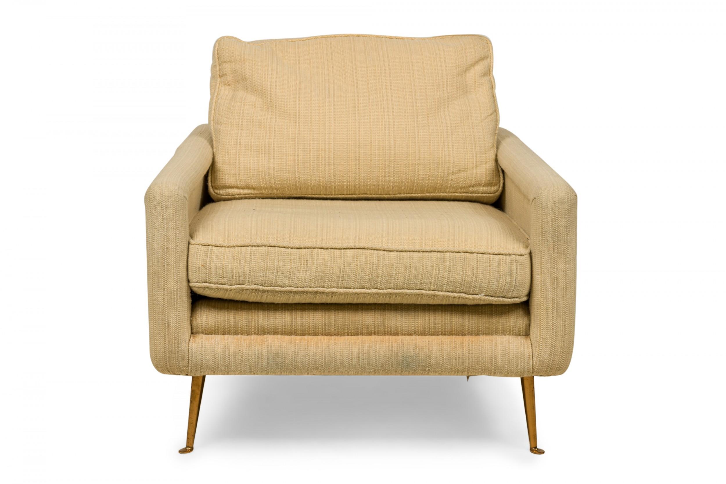 American Contemporary lounge / armchair with textured beige fabric upholstery with removable back and seat cushions resting on four tapered bronze legs ending in circular feet.