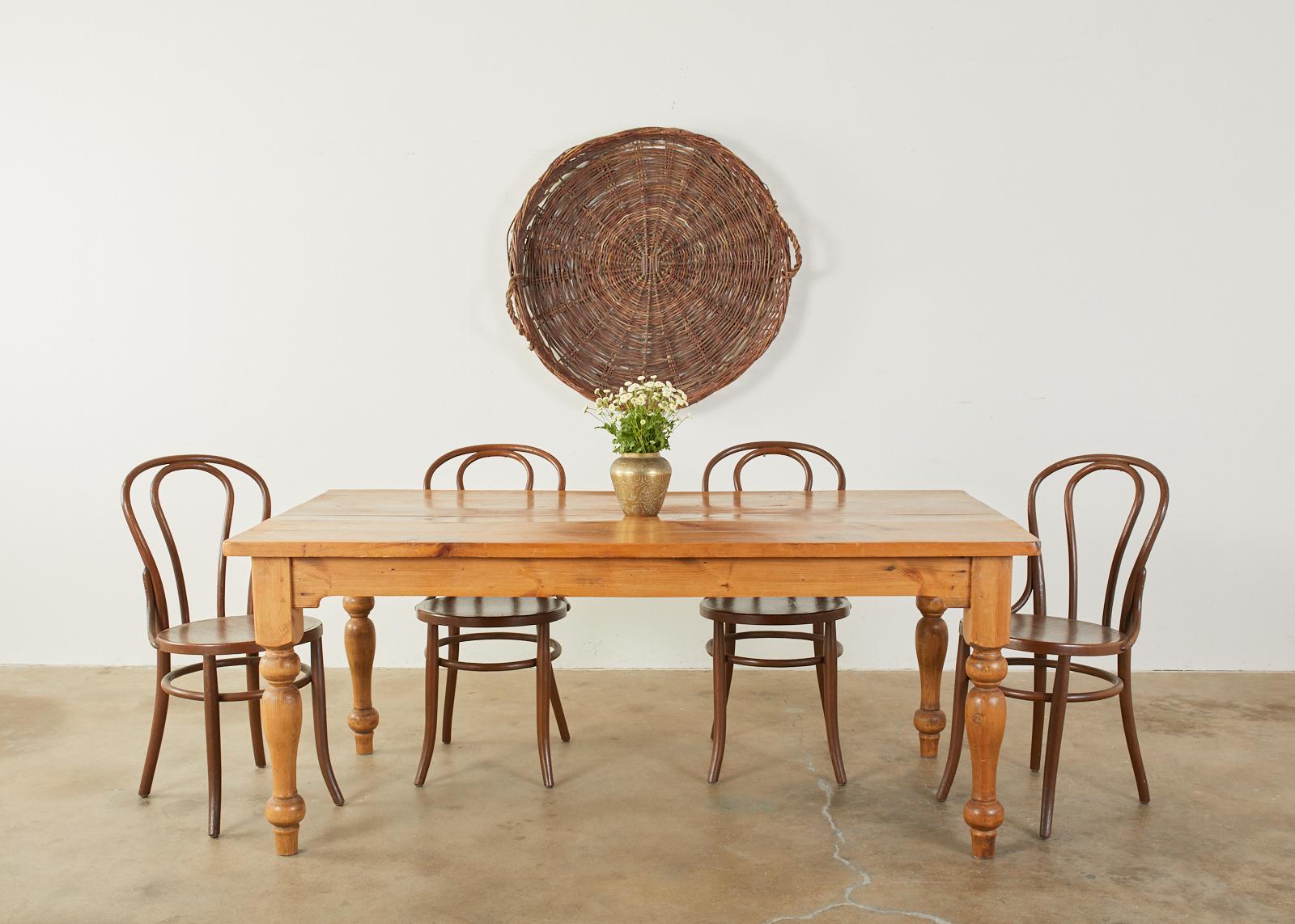 Rustic American country farmhouse harvest table or dining table. Features a thick plank top with a warm honey pine patina. Supported by thick, chunky turned legs ending with a peg foot. Ample leg room with 25 inches from the apron to the floor.