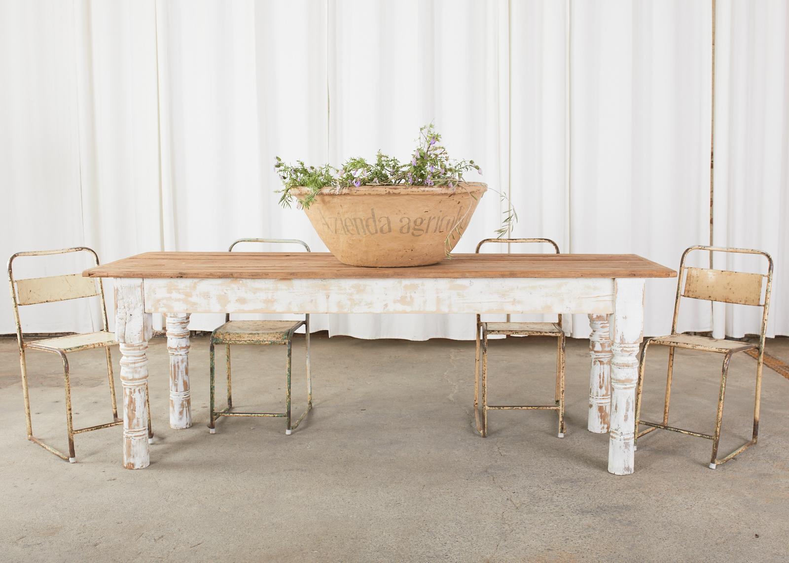 Rustic American country style farmhouse dining table or harvest table crafted from reclaimed pine. The table top features weathered planks of barn wood with breadboard ends. Supported by thick, chunky turned legs measuring 4 inches thick. The turned