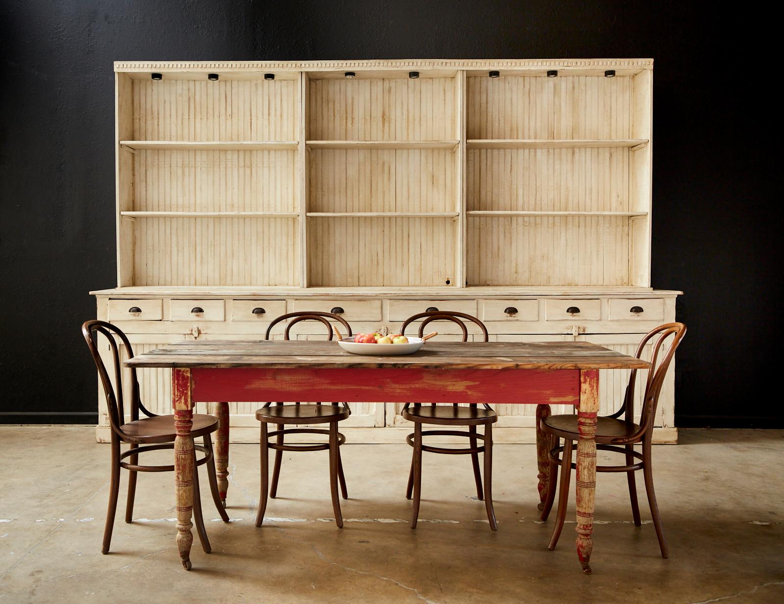 Rustic American country pine farmhouse dining table on casters. Featuring a four wood plank top with rounded corners. Supported by a red painted base. The farm table has round turned legs ending with metal casters. Lovely distressed aged patina with